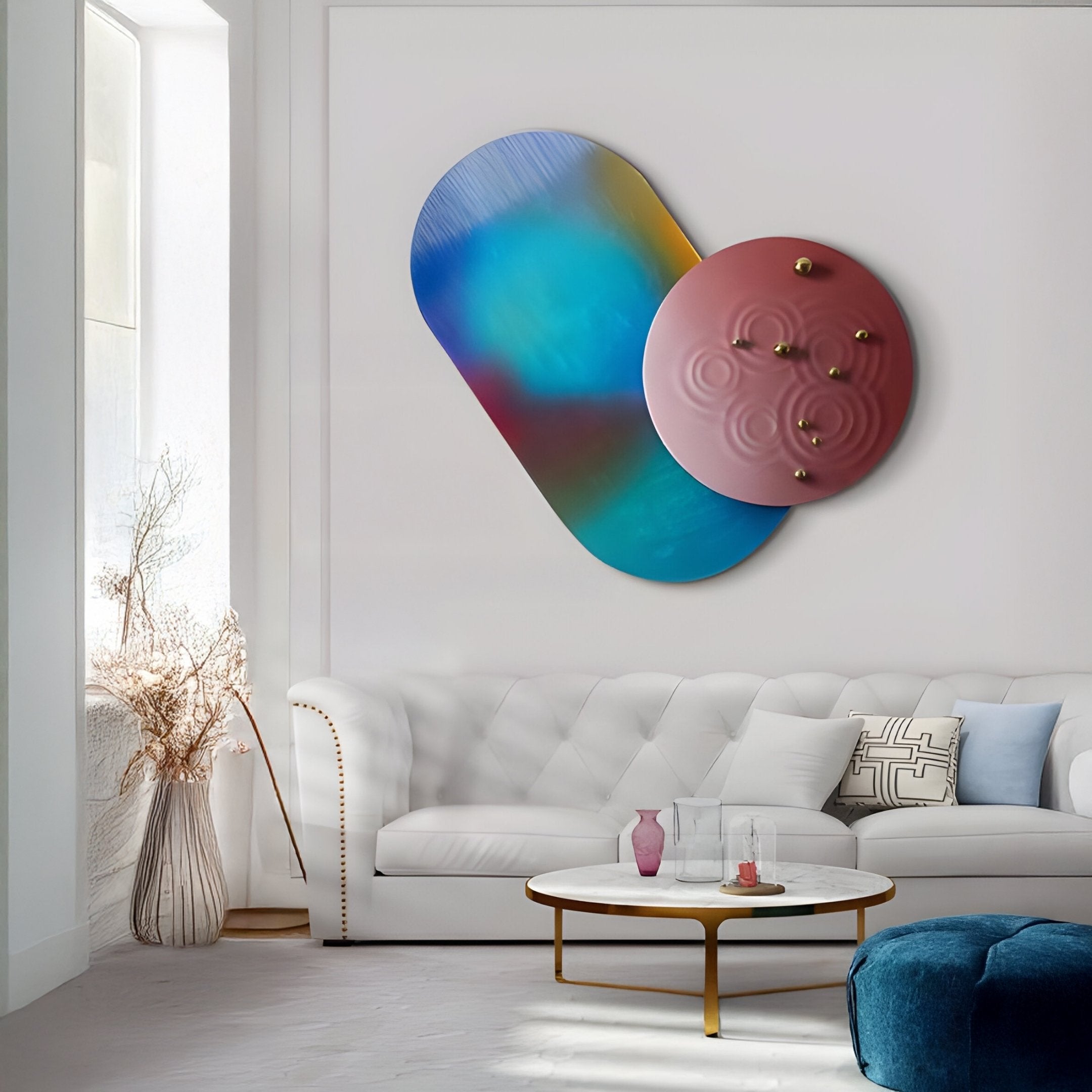 A modern living room showcases a white tufted sofa with blue and white pillows, a round coffee table with a gold base, and the Embera Abstract Circle Deep Burgundy & Teal 3D Wall Art by Giant Sculptures. A vase with dried plants by the window completes this contemporary statement piece.
