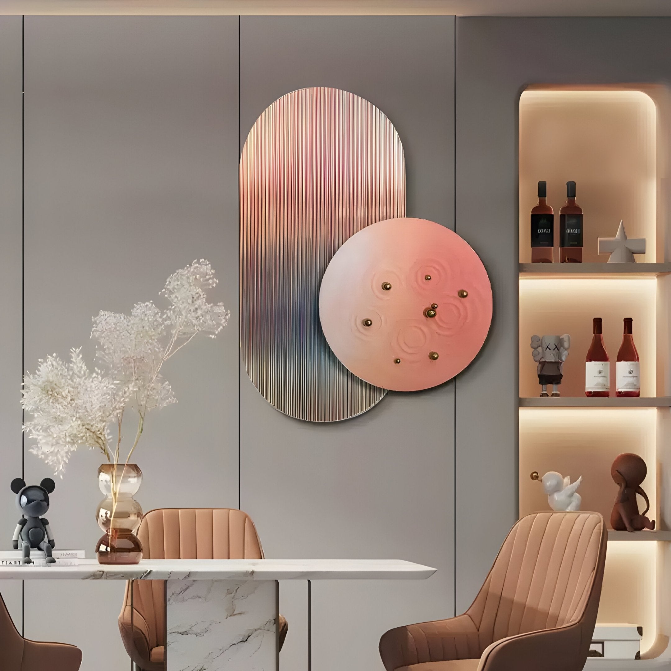 A modern dining area features a marble table with tan chairs and the Embera Abstract Circle Warm Blush Gradient 3D Wall Art by Giant Sculptures on a gray paneled wall. Backlit shelves showcase wine bottles and decor, while a vase with white flowers adds elegance to the scene.