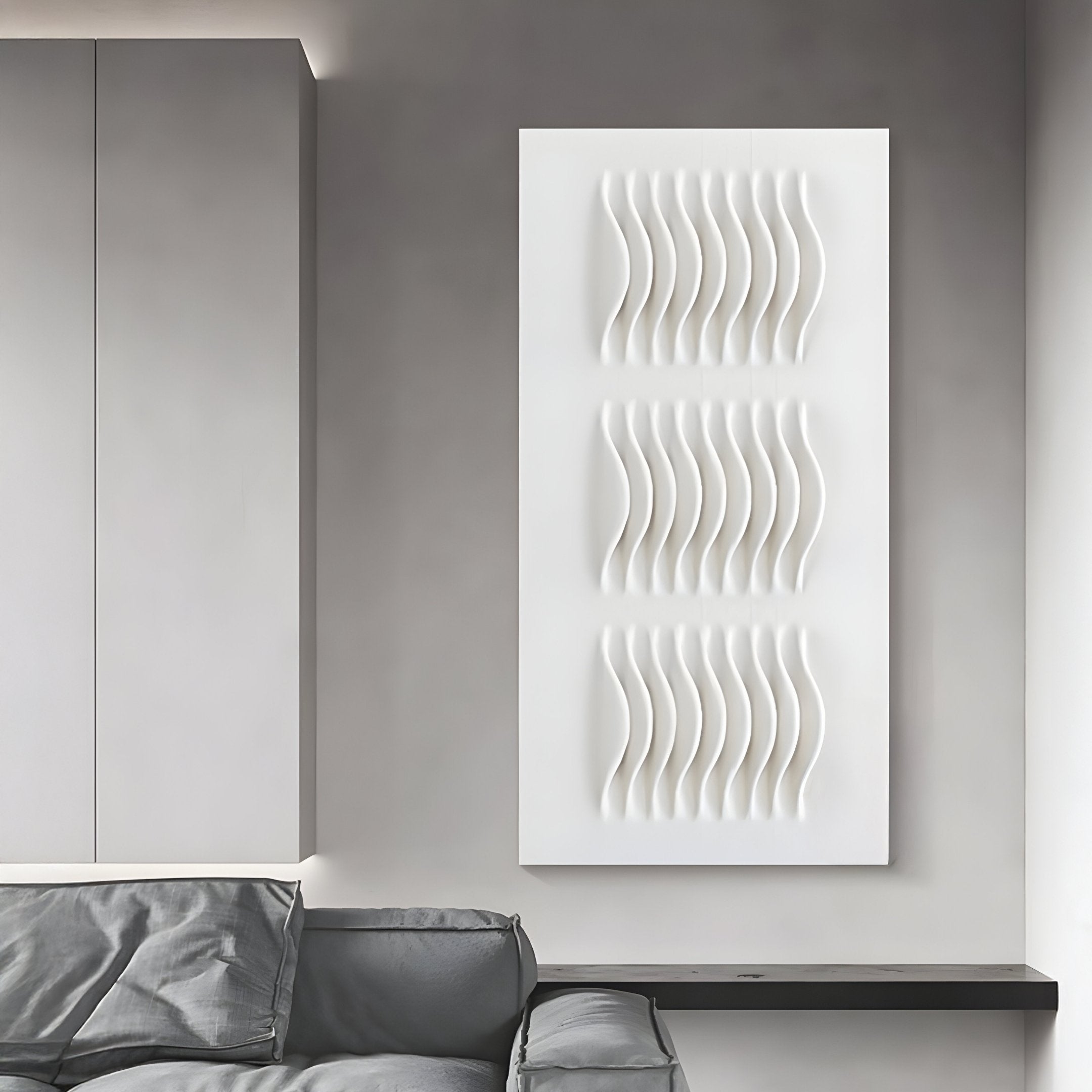 A modern living room includes a light gray sofa with matching cushions. On the wall, the Giant Sculptures Ondara Wave White Vertical Wood Relief 3D Wall Art displays three wavy sections, offering a minimalist and textured art piece against the gray backdrop.