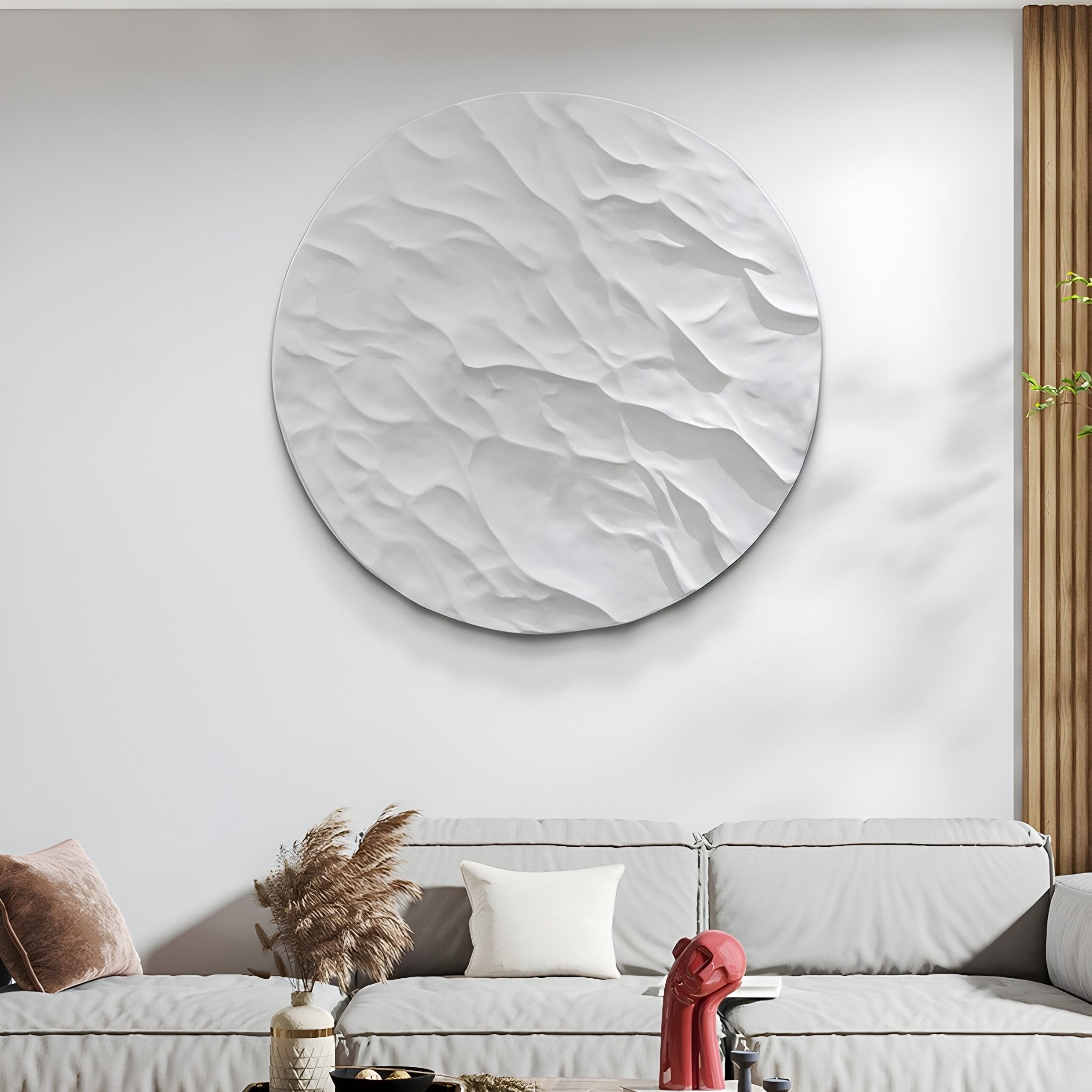The Orenda Subtle Wave White Wood Relief 3D Wall Art by Giant Sculptures is mounted above a modern gray sofa. This Japanese-inspired design features beige and white cushions, and a vase of dried plants sits on the minimalist coffee table in front.