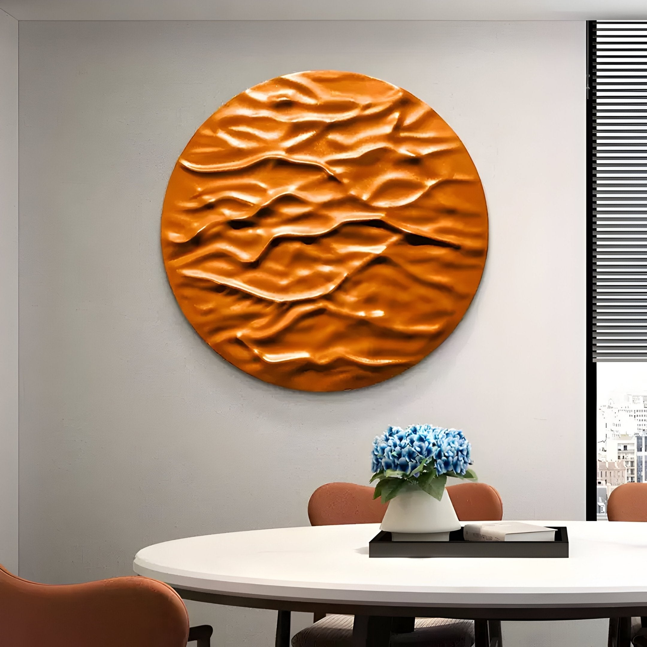 The Orenda Ripple Wave Orange Wood Relief 3D Wall Art by Giant Sculptures graces a gray wall above a white table with a blue-flowered vase, encircled by light brown chairs. Partially open blinds on the window reveal a cityscape.
