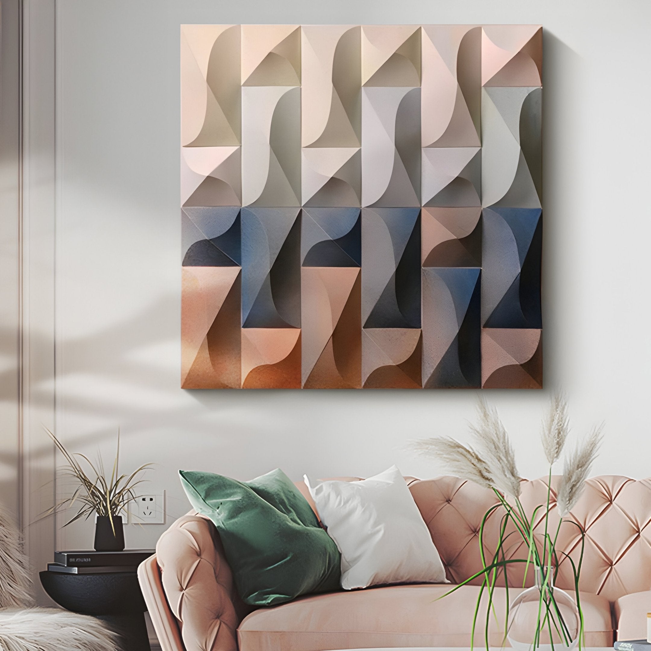 A contemporary living room includes a blush pink tufted sofa with white and green pillows. On the white wall above hangs an Elysia Geometric Warm Gradient Wood Relief 3D Wall Art by Giant Sculptures, in beige, blue, and brown. Pampas grass and a clay pot complete the scene.