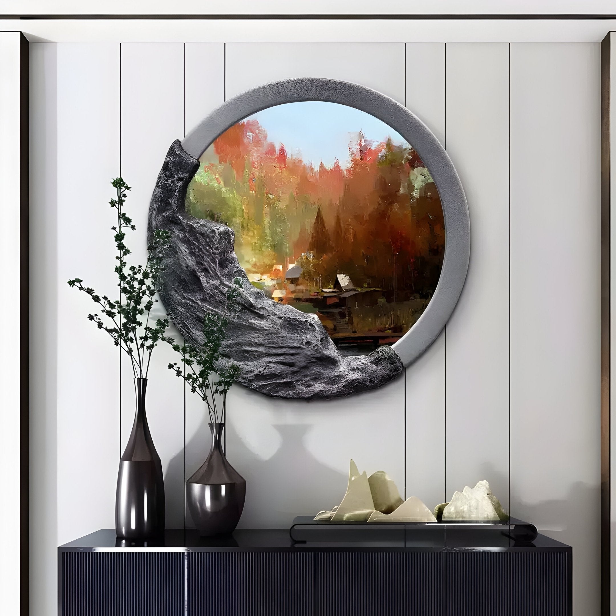 A round decorative mirror, reminiscent of a Sylvara Autumn Woods landscape with trees and a building, is mounted on the wall. The frame has a textured design on one side. Below, Giant Sculptures 3D wall art vases with branches and abstract sculptures elegantly sit on a black console table.