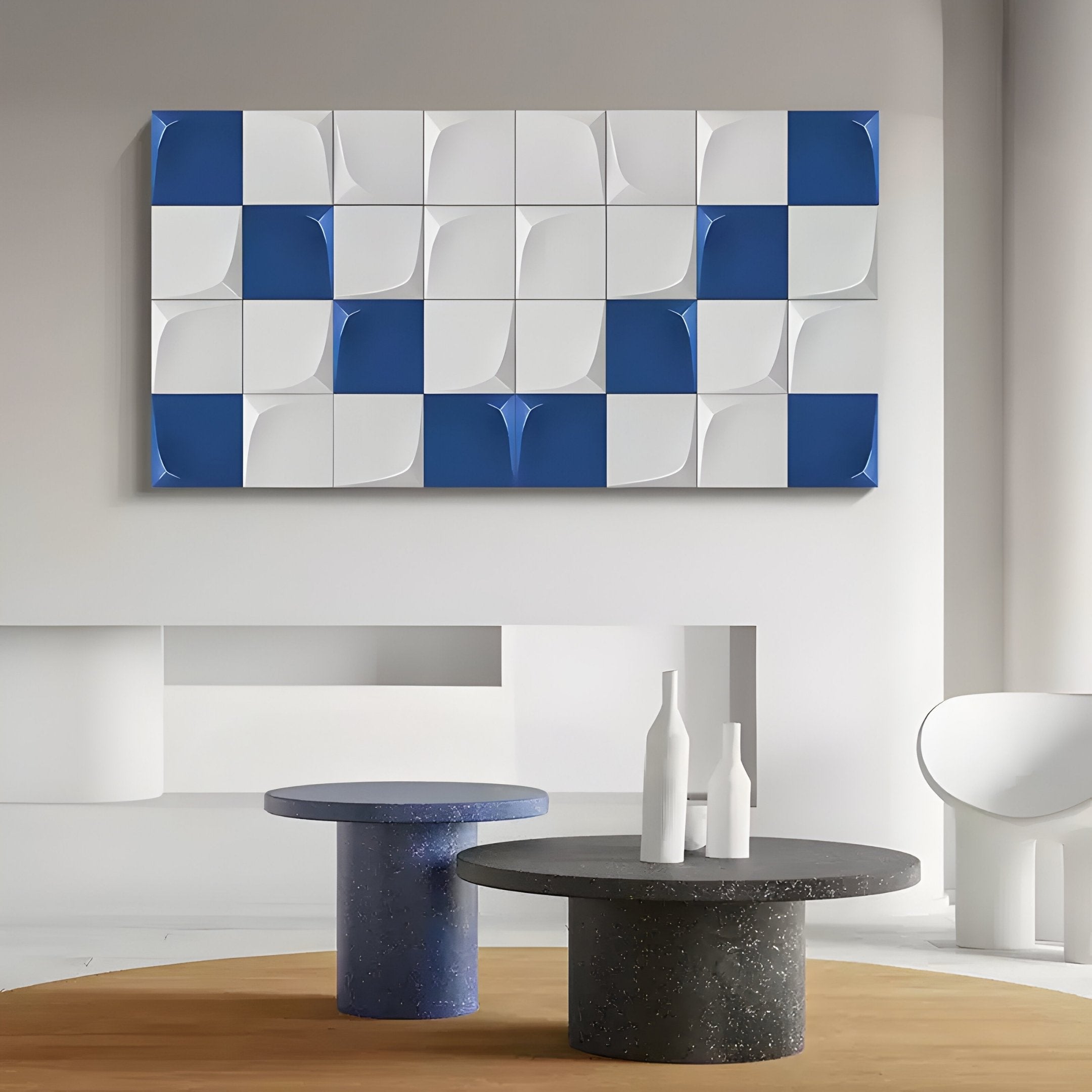 A modern art gallery features a stunning Averra White & Blue Geometric Wood Relief 3D Wall Art by Giant Sculptures. Two round tables with decorative white bottles enhance the contemporary decor against minimalist gray and white walls with curved elements.