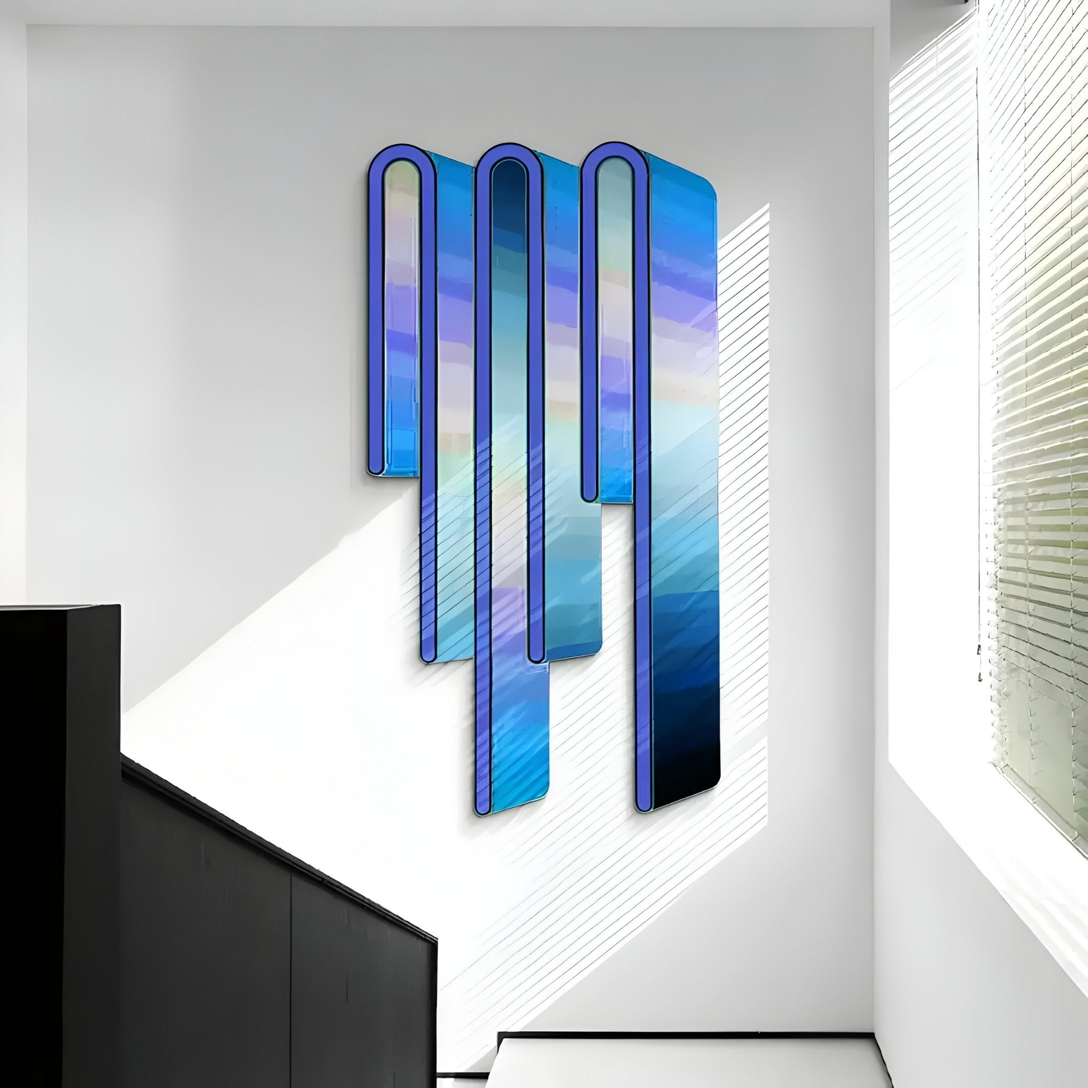 The Opaline Twilight Azure Gradient Wood Relief 3D Wall Art by Giant Sculptures features elongated vertical panels in blue and purple hues, casting shadows on a white wall in natural light. A staircase with a black railing is partially visible.