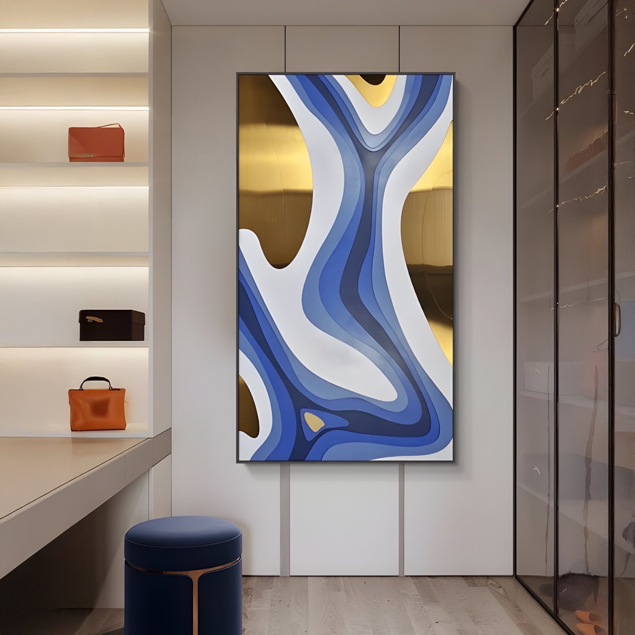 A modern room features a stunning Marea Organic Flow Blue & Gold Wood Relief 3D Wall Art by Giant Sculptures, with its captivating swirls. Chic handbags are displayed on left shelves, a glass cabinet stands to the right, and a blue stool rests gracefully on the wooden floor.
