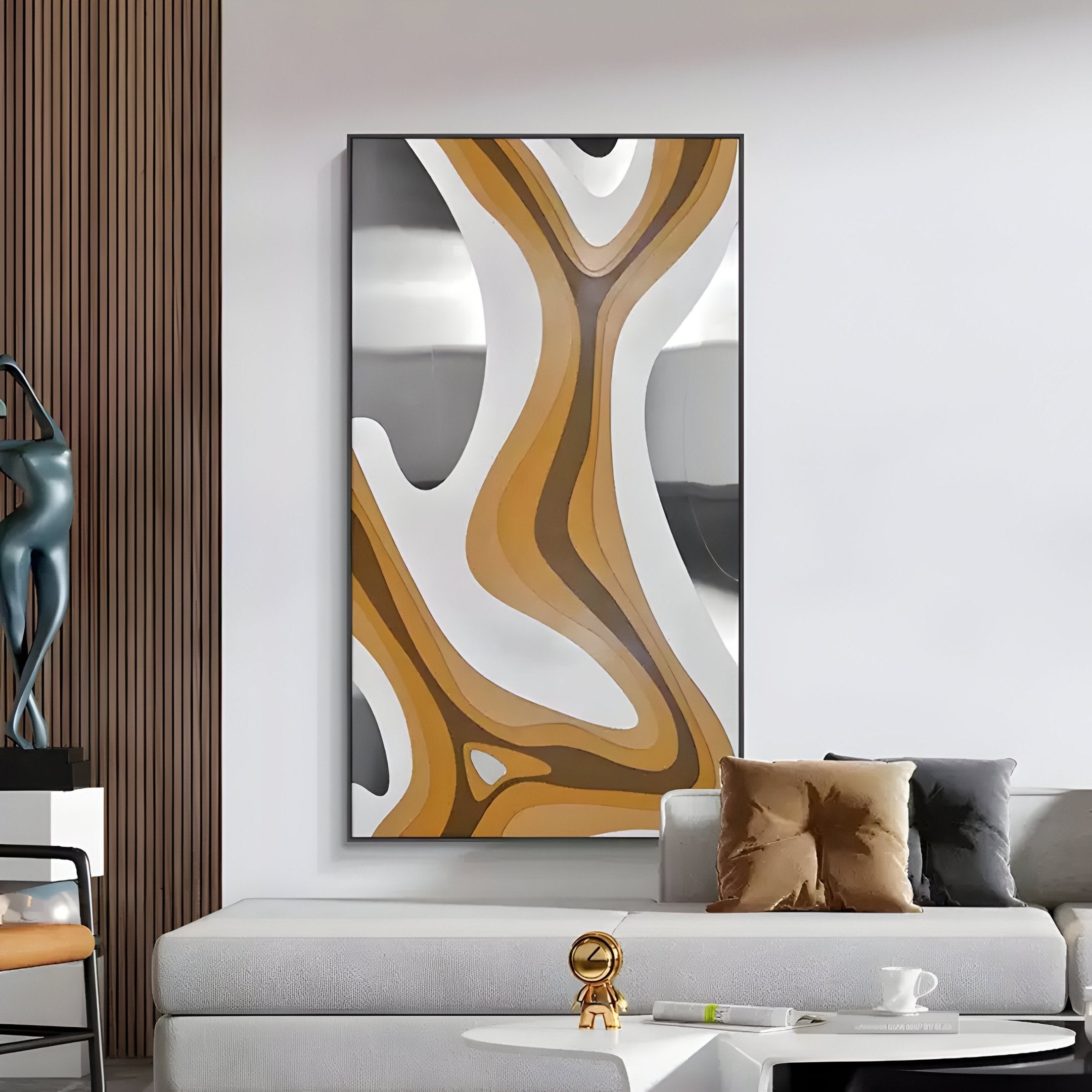 A modern living room showcases the Marea Organic Flow Ochre & Silver Wood Relief 3D Wall Art by Giant Sculptures, featuring abstract shapes in brown, white, and black. A grey couch with brown and grey cushions sits next to a gold sculpture on a white table, while a wood art statue is partially visible.