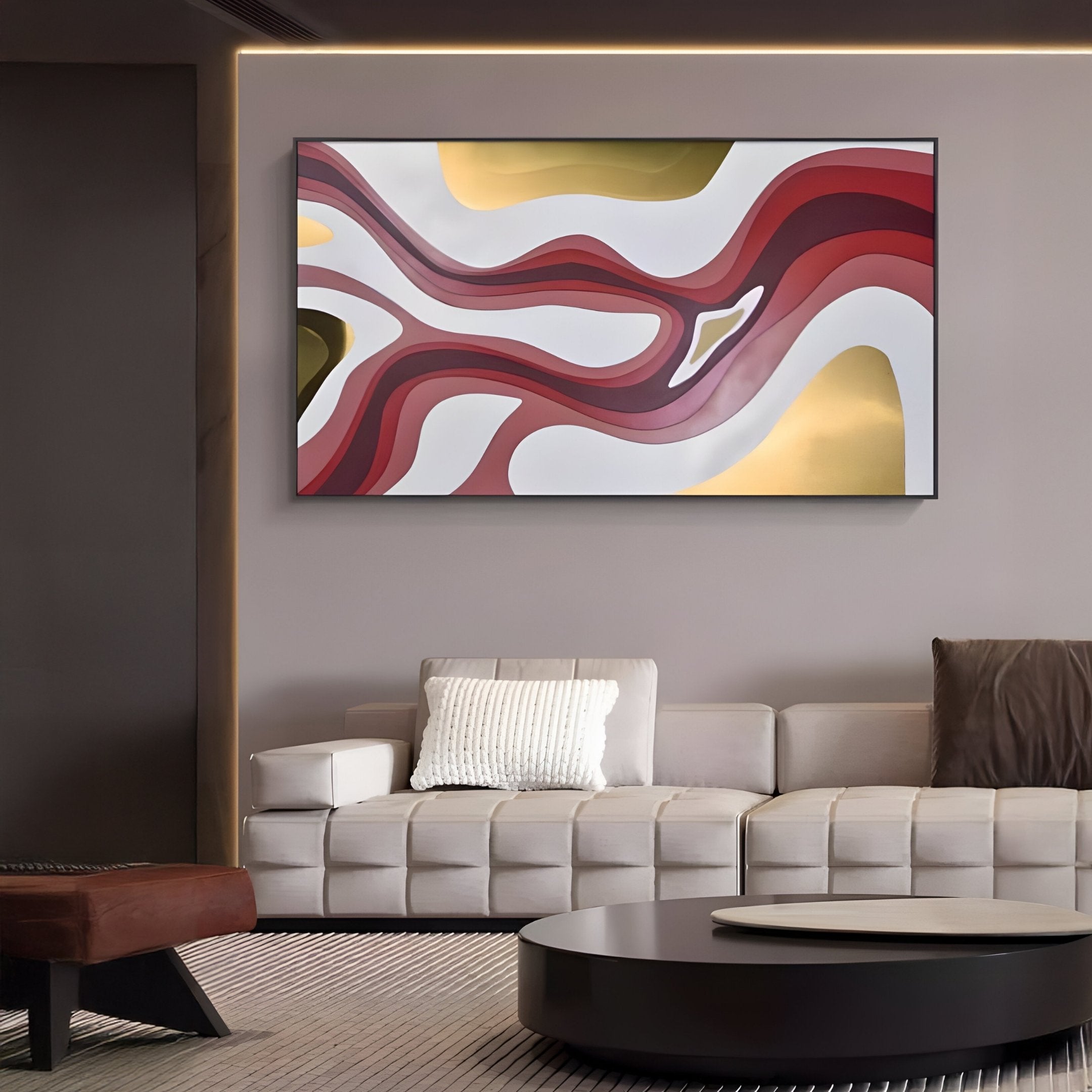 A striking Marea Organic Flow Crimson & Gold Wood Relief 3D Wall Art by Giant Sculptures adorns the wall above a modern beige couch. A textured white pillow and a dark round coffee table with a brown ottoman complete the warm, minimalistic room decor.