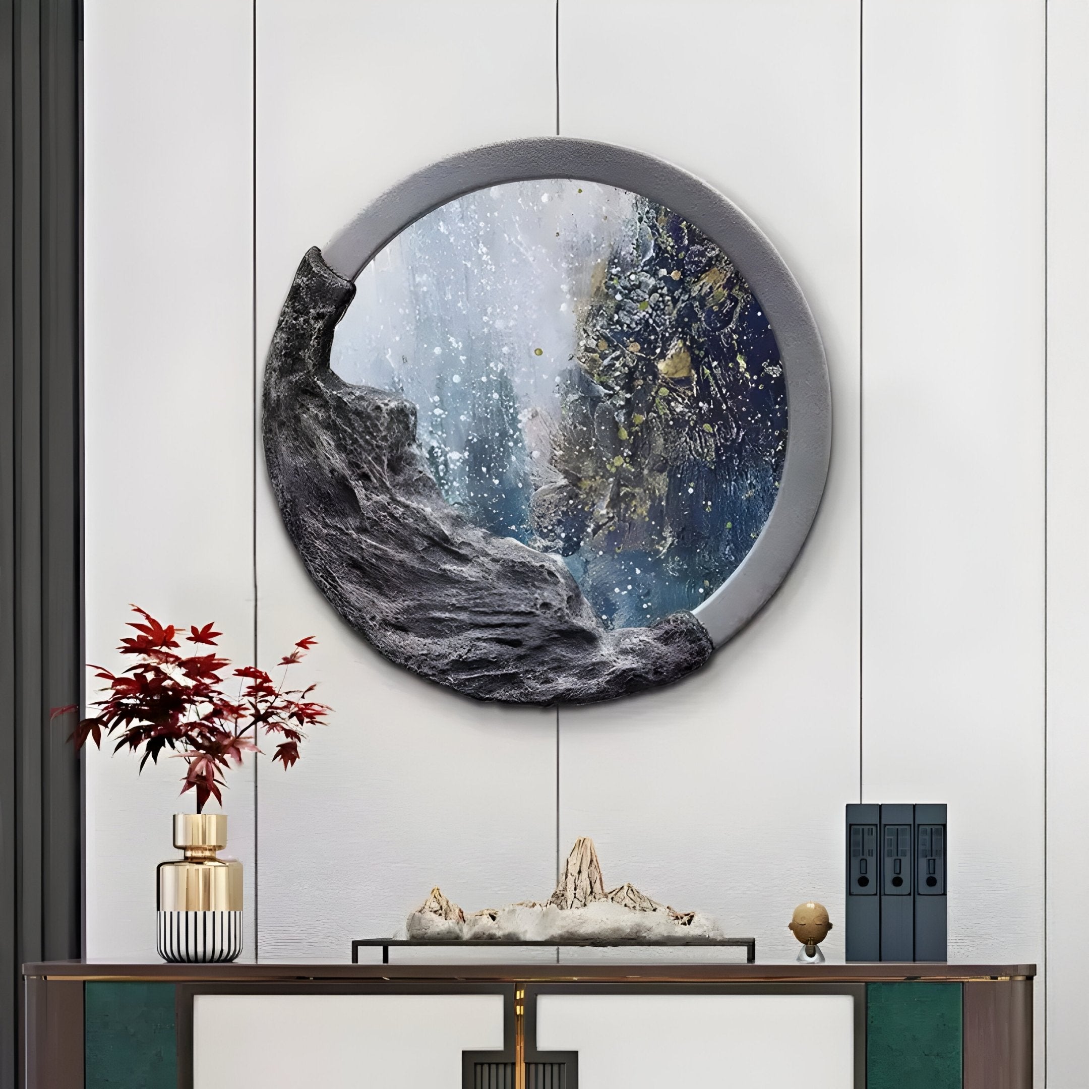 A modern interior showcases a circular wall mirror with an abstract ocean wave design reminiscent of the Auroria Coastal Whisper by Giant Sculptures. Below, a wooden console displays a bonsai-style plant, decorative items, and books against a white-paneled wall.