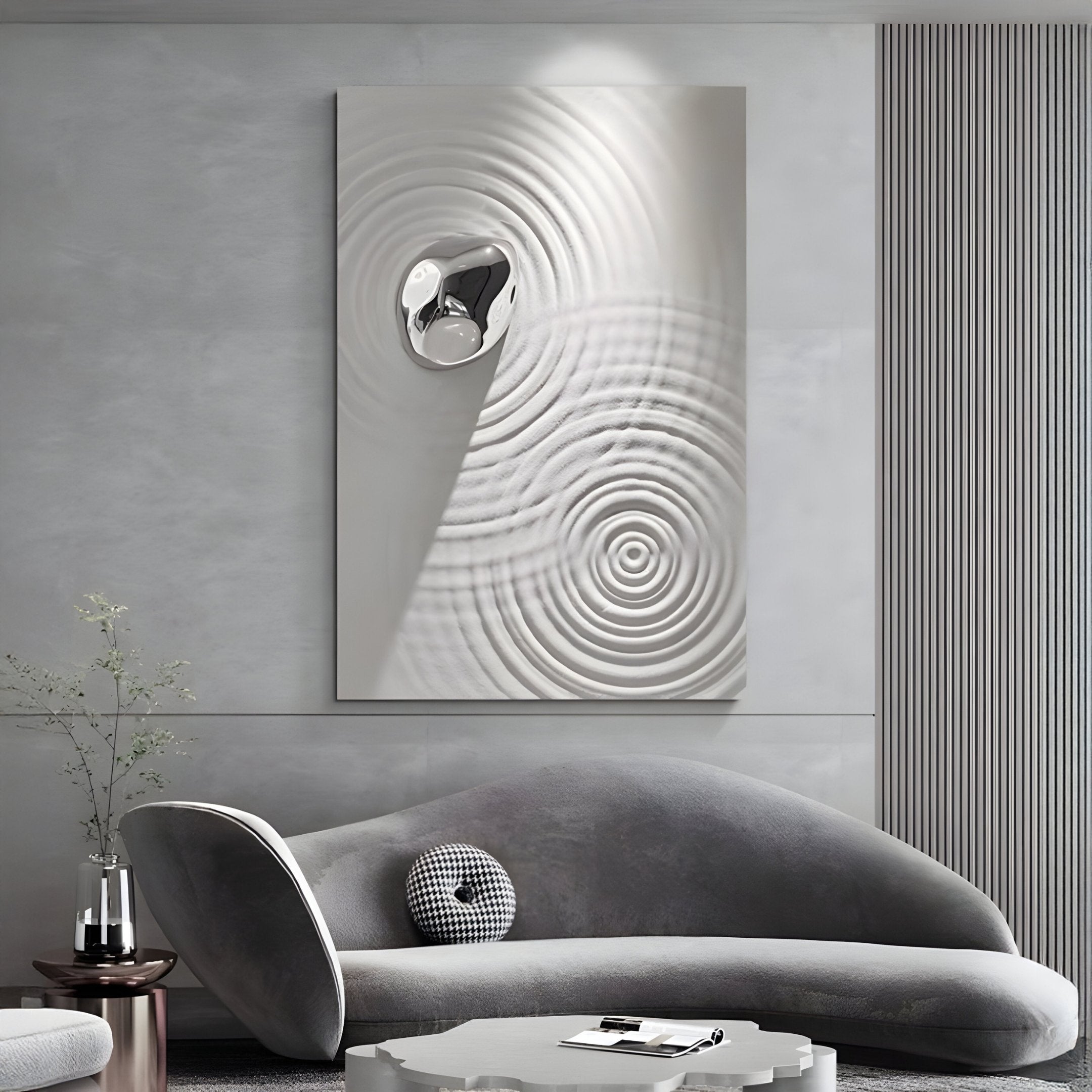 A modern living room features a curved gray sofa with a pillow, a white coffee table, and the Ondella Silver Ripple I 3D Wall Art by Giant Sculptures on the wall. A plant vase near the sofa enhances the minimalist decor.