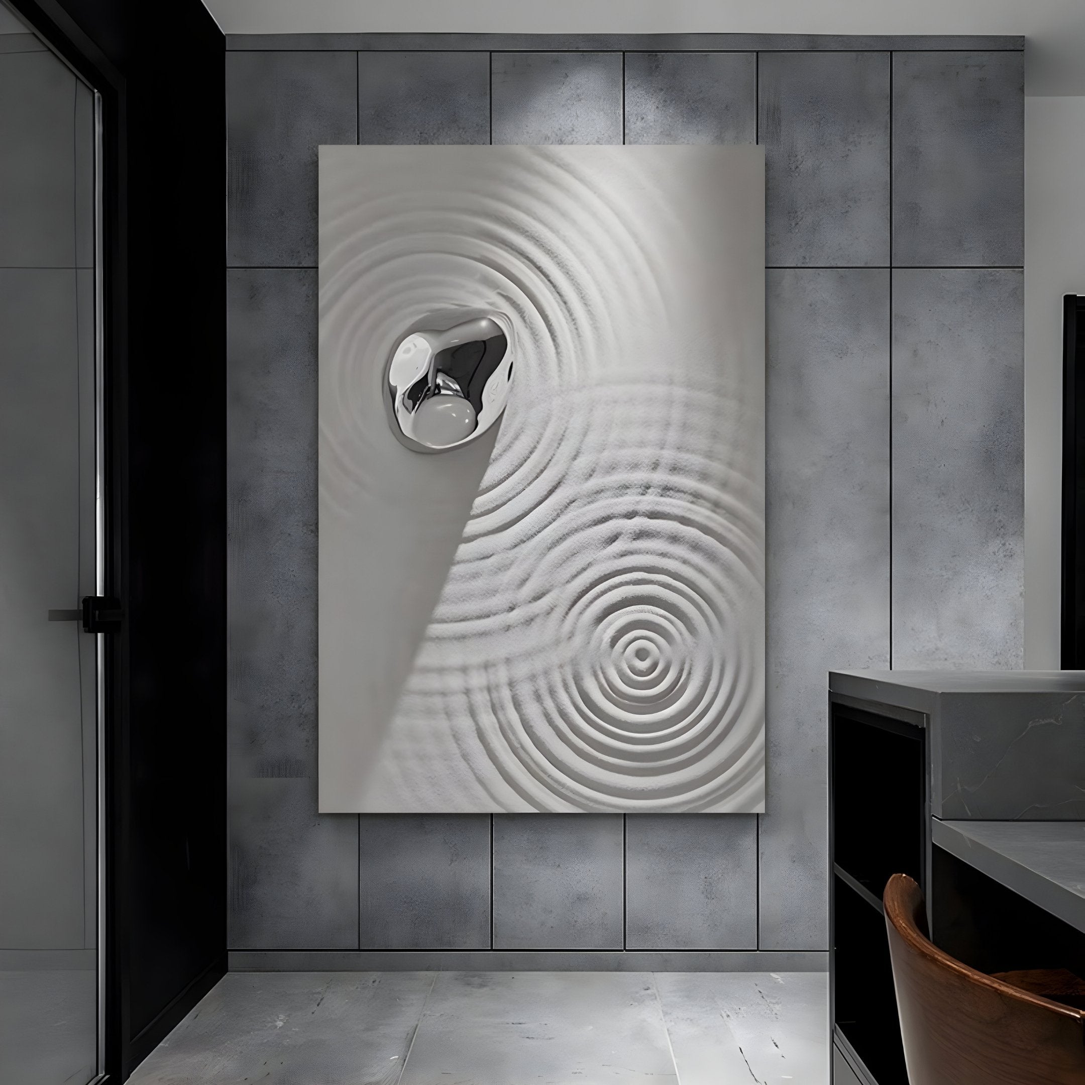 A modern room showcasing the Ondella Silver Ripple I Sandstone Wood Relief 3D Wall Art by Giant Sculptures, featuring large abstract circular patterns with a shiny metallic center. The industrial gray wall complements the minimalist decor, and a wooden chair is partially visible.