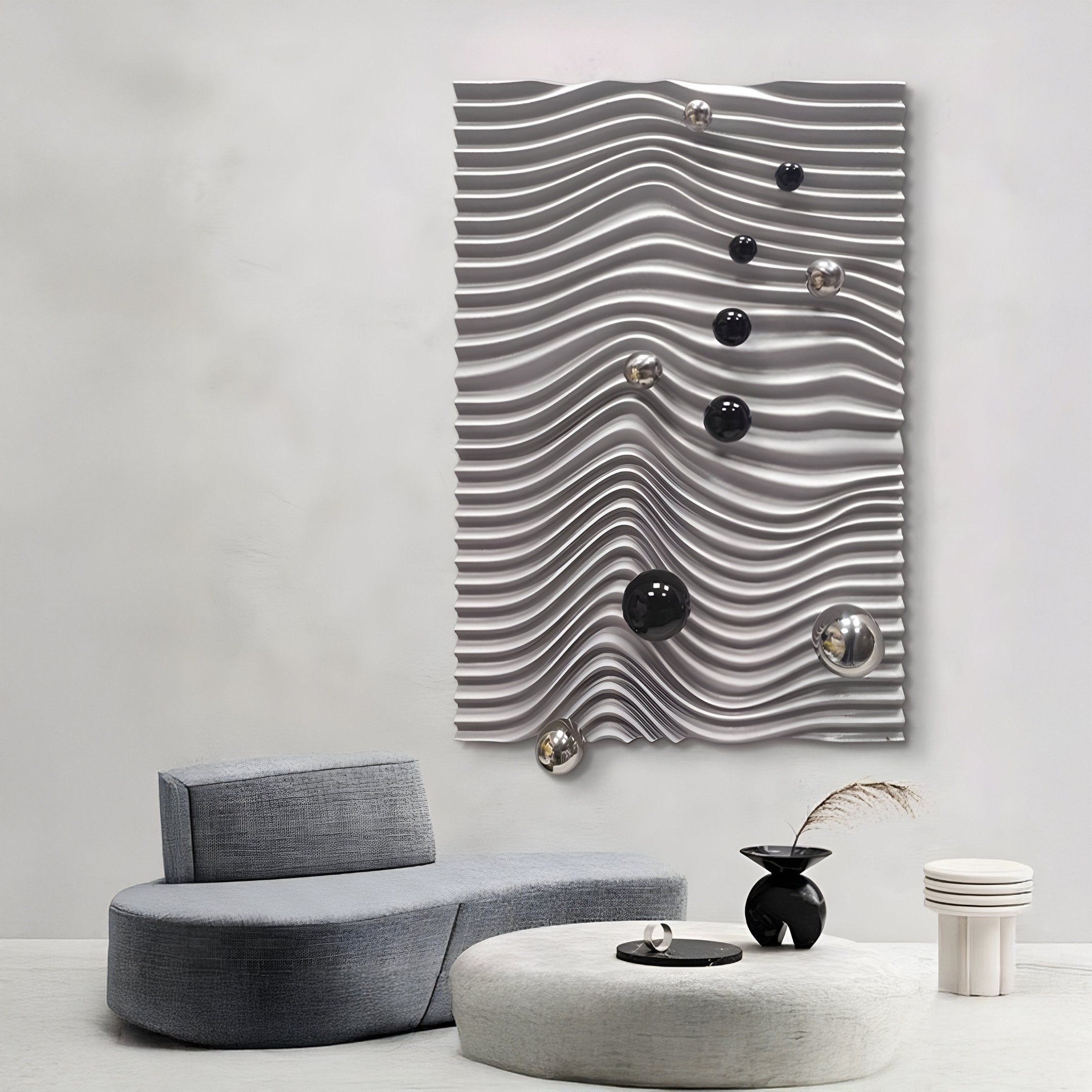 Experience modern interiors with the Calidora Wave Sculpted 3D Relief Wall Art by Giant Sculptures featuring black and silver spheres. A curved gray sofa graces the light floor, paired with a small black vase and white stacked side table, ideal for contemporary decor enthusiasts.