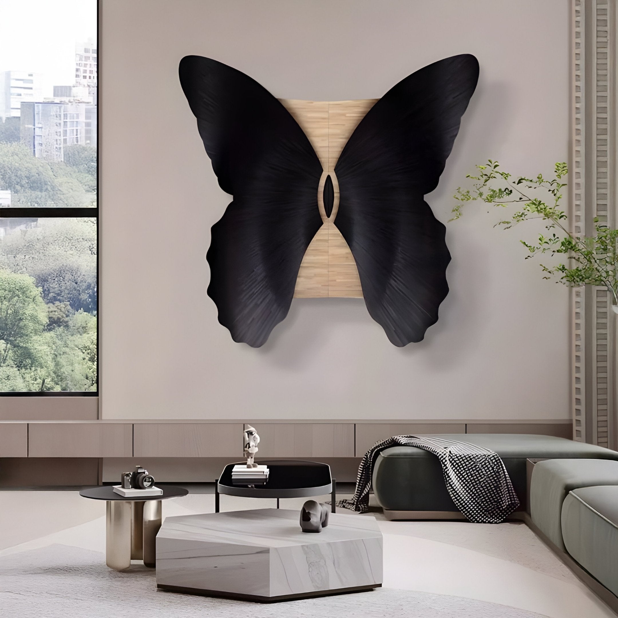 A modern living room includes the striking Lucerna Black Butterfly Wood Carving 3D Wall Art by Giant Sculptures. A gray sectional sofa with a patterned pillow, a small table with decor items, and tall windows showcasing greenery complete the space.