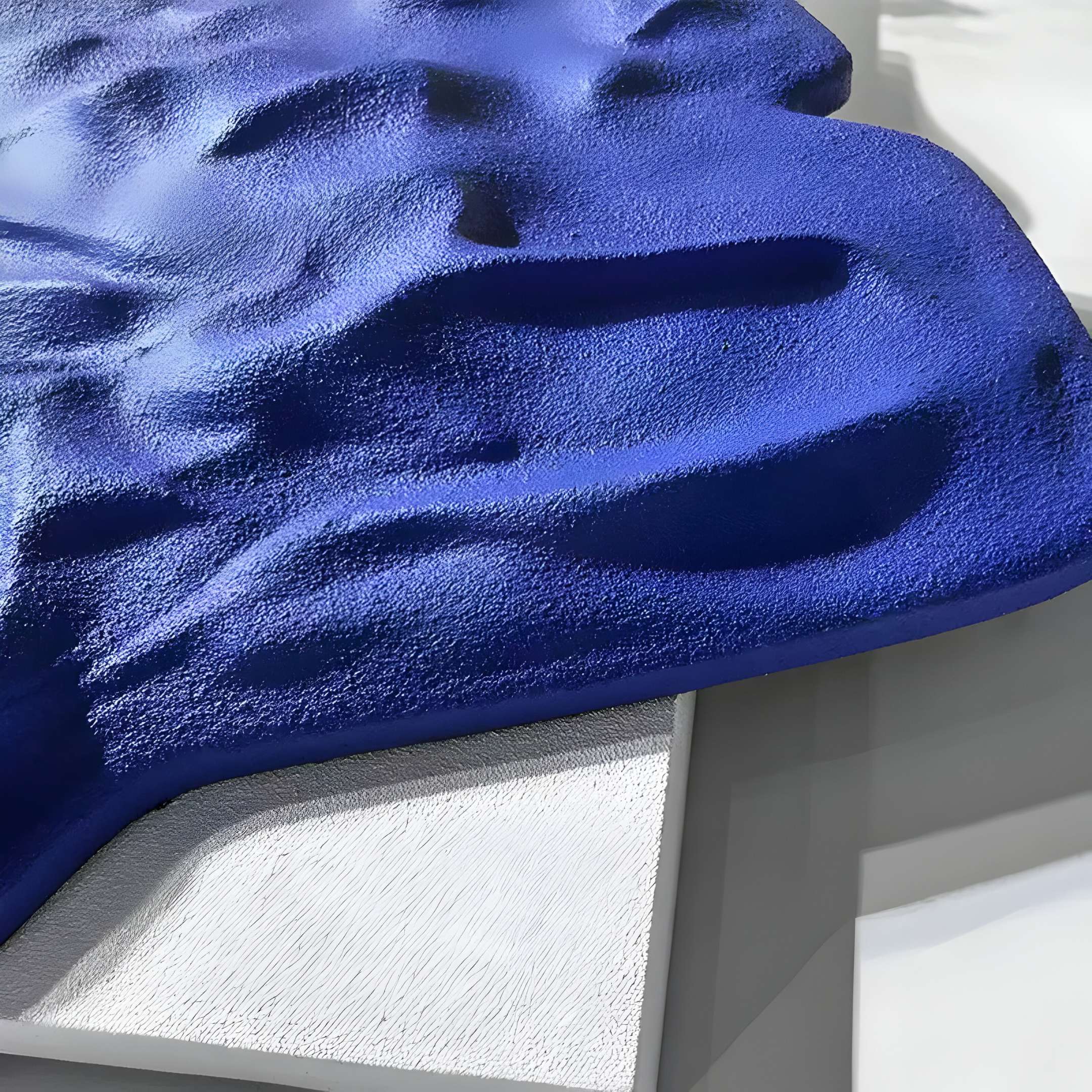 A textured Veritas White & Sapphire Blue Wood Relief by Giant Sculptures drapes over a surface, echoing 3D Wall Art. Shadows highlight its velvety depth, while the uneven texture adds dynamic movement.