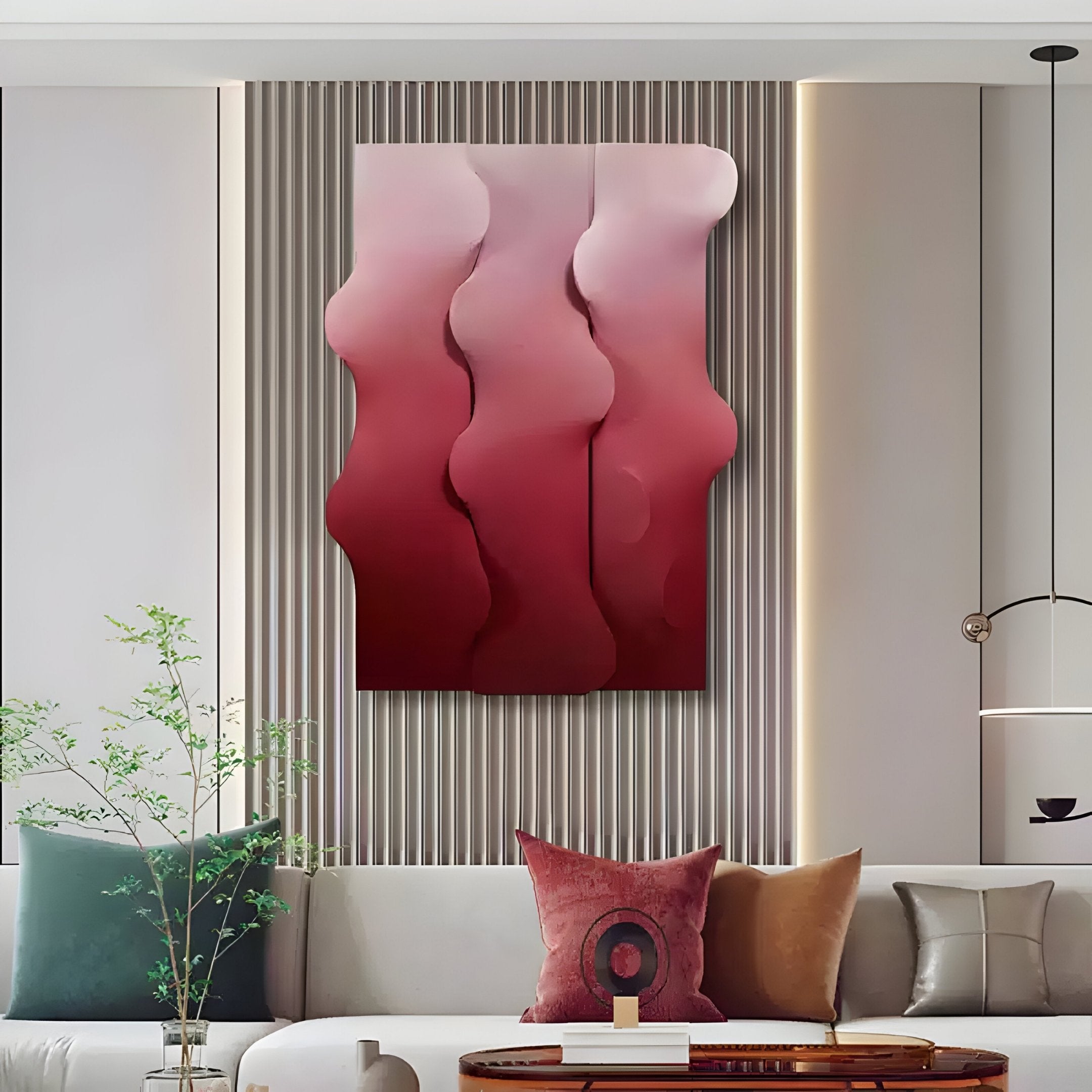 A modern living room features a beige sofa with accent pillows, a small round wooden table, and a potted plant. Above the sofa hangs Giant Sculptures Mystique Red Fabric Abstract Wood Relief 3D Wall Art displaying wavy shapes in pink and red against a striped wall.