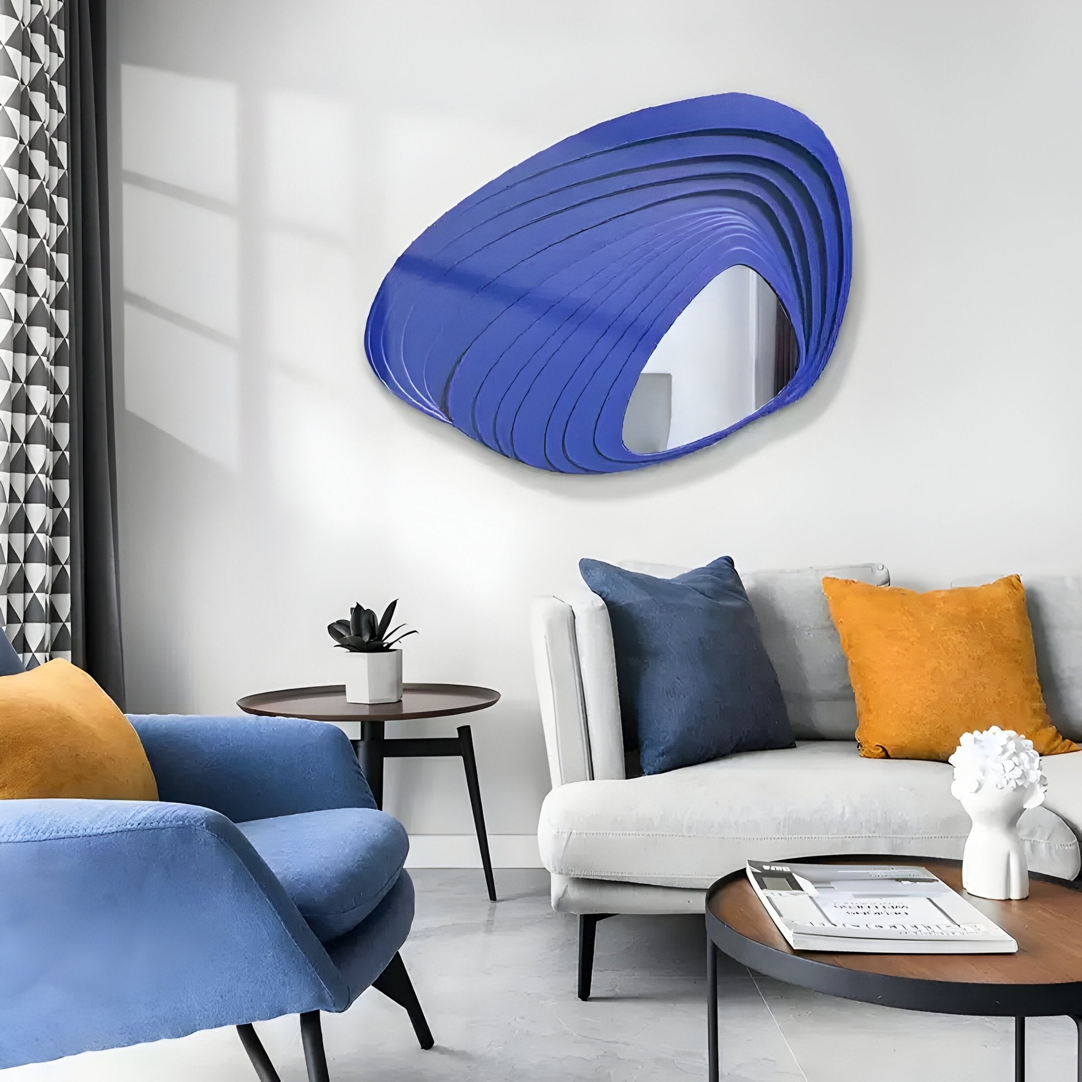 A modern living room showcases the Reflecta Blue Wood Carving Mirror 3D Wall Art by Giant Sculptures. A blue armchair and cream sofa with yellow pillows surround round tables. Geometric curtains and small plants add stylish accents to this elegant space.