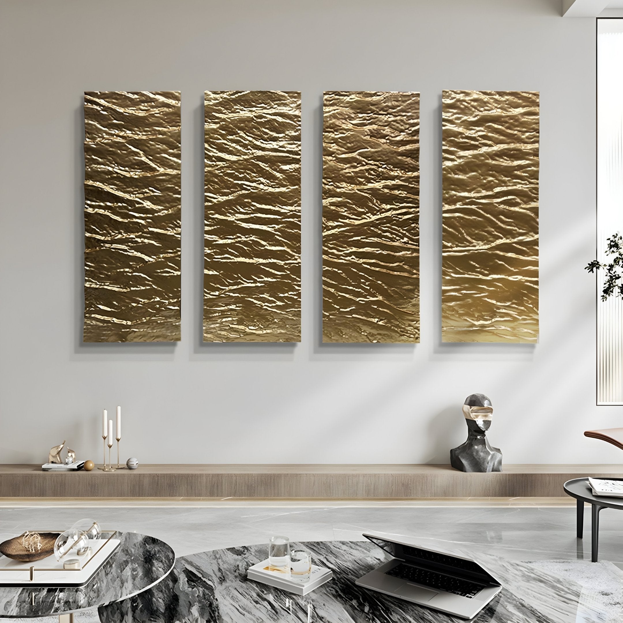 A modern living room boasts four Illume Gold IV Hand-Painted Wood Relief 3D Wall Art panels by Giant Sculptures on a white wall. A wooden shelf displays candles and decor items. Nearby, a laptop and glass sit on a marble table, with a decorative bust wearing headphones adding character.
