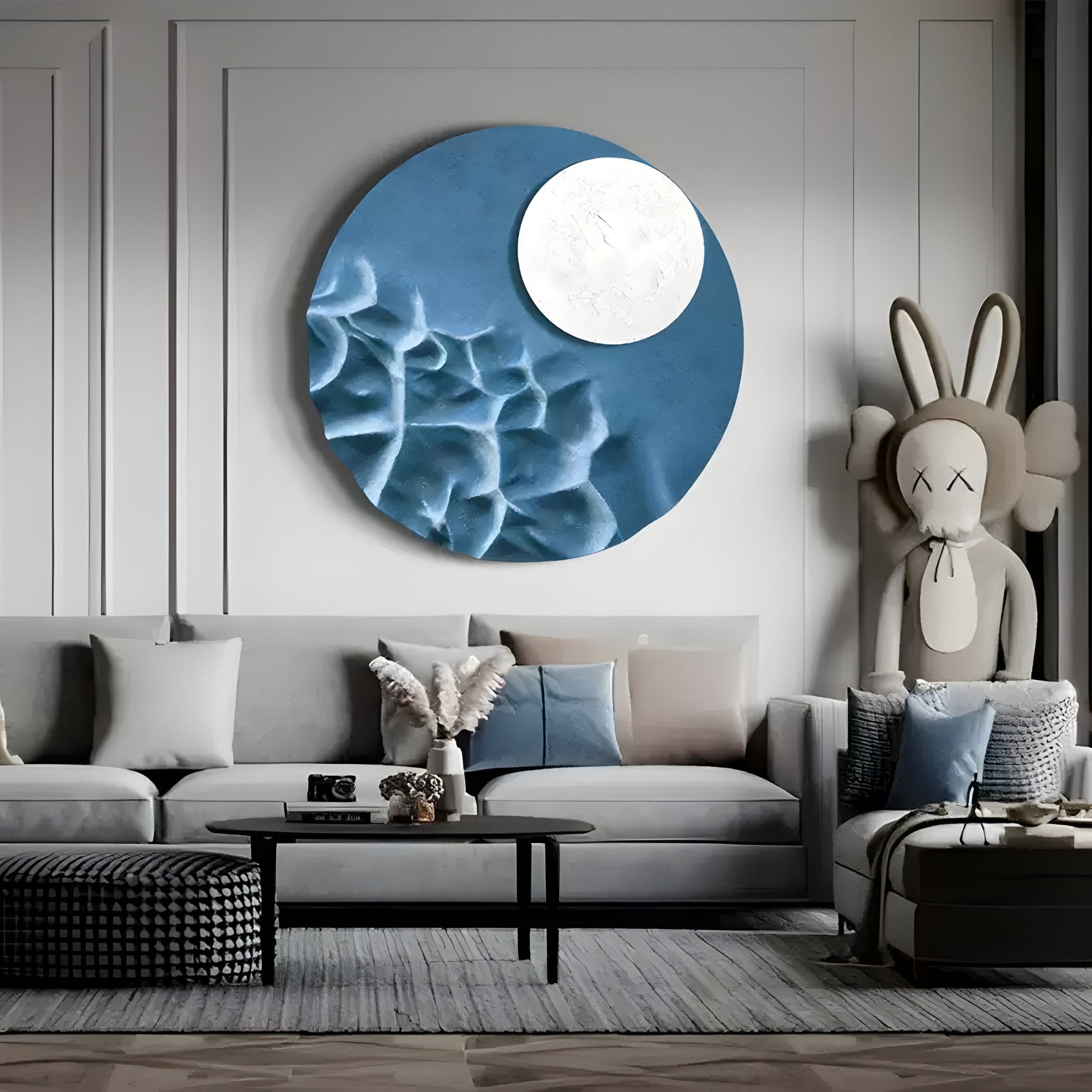 A modern living room showcases the Verve Soft Blue Wood Relief 3D Wall Art by Giant Sculptures above a beige sofa with assorted cushions. A plush bunny is seated on the right, while a black coffee table and checkered ottoman enhance the decor, complemented by soft blue wood relief accents.