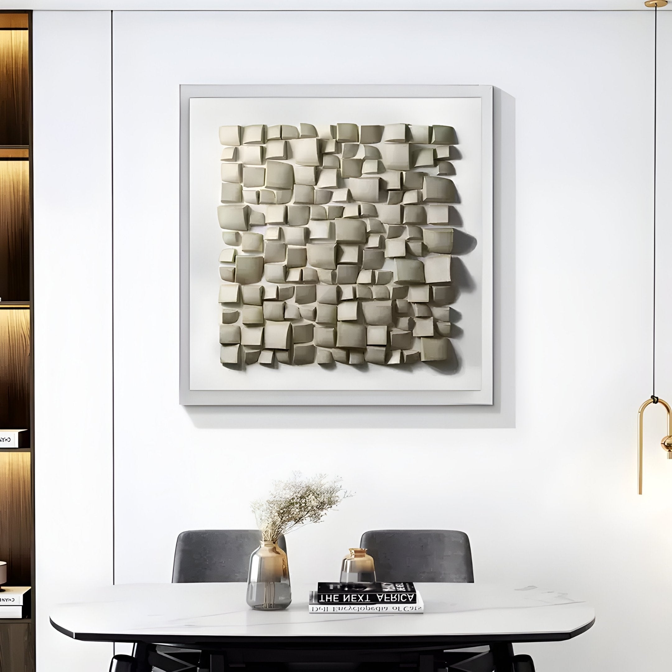 A modern dining area exudes wabi-sabi charm with a white wall featuring Exalta Wood Relief 3D Wall Art by Giant Sculptures. Below, a table holds dried flower vases and books, flanked by gray chairs. A pendant light hangs right, with Exalta wood relief shelves to the left.