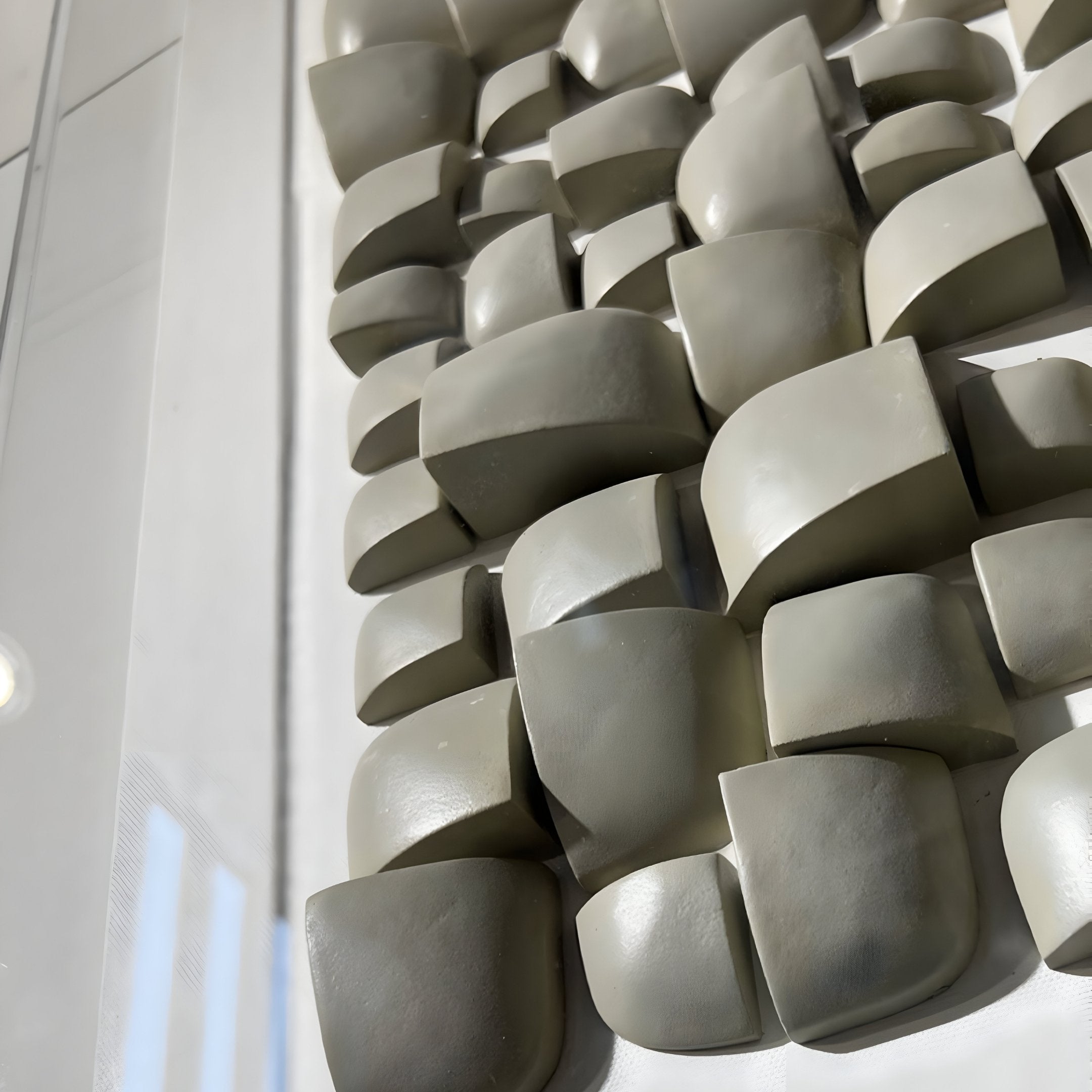 The Exalta Wood Relief 3D Wall Art by Giant Sculptures features smooth, light gray blocks in a wave pattern. Its curved surfaces play with light for subtle shadows and highlights, embodying a wabi-sabi aesthetic within an acrylic box that captures perfectly imperfect elegance.
