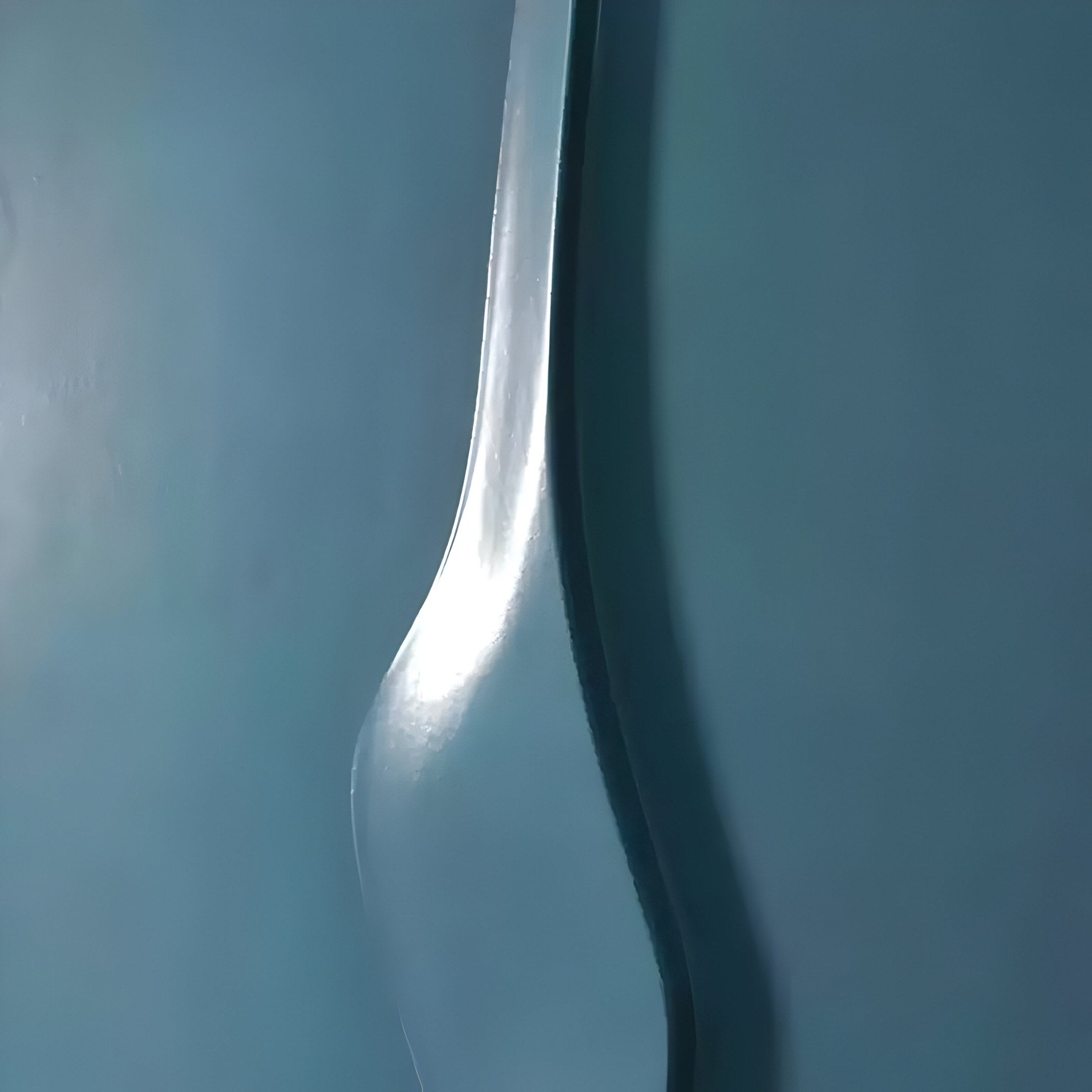 The Velar Vertical Blue Wood Carving 3D Wall Art by Giant Sculptures is a metallic, abstract piece with wavy designs. It reflects light against a smooth teal wall, creating soft highlights and shadows that accentuate its curvature and texture.