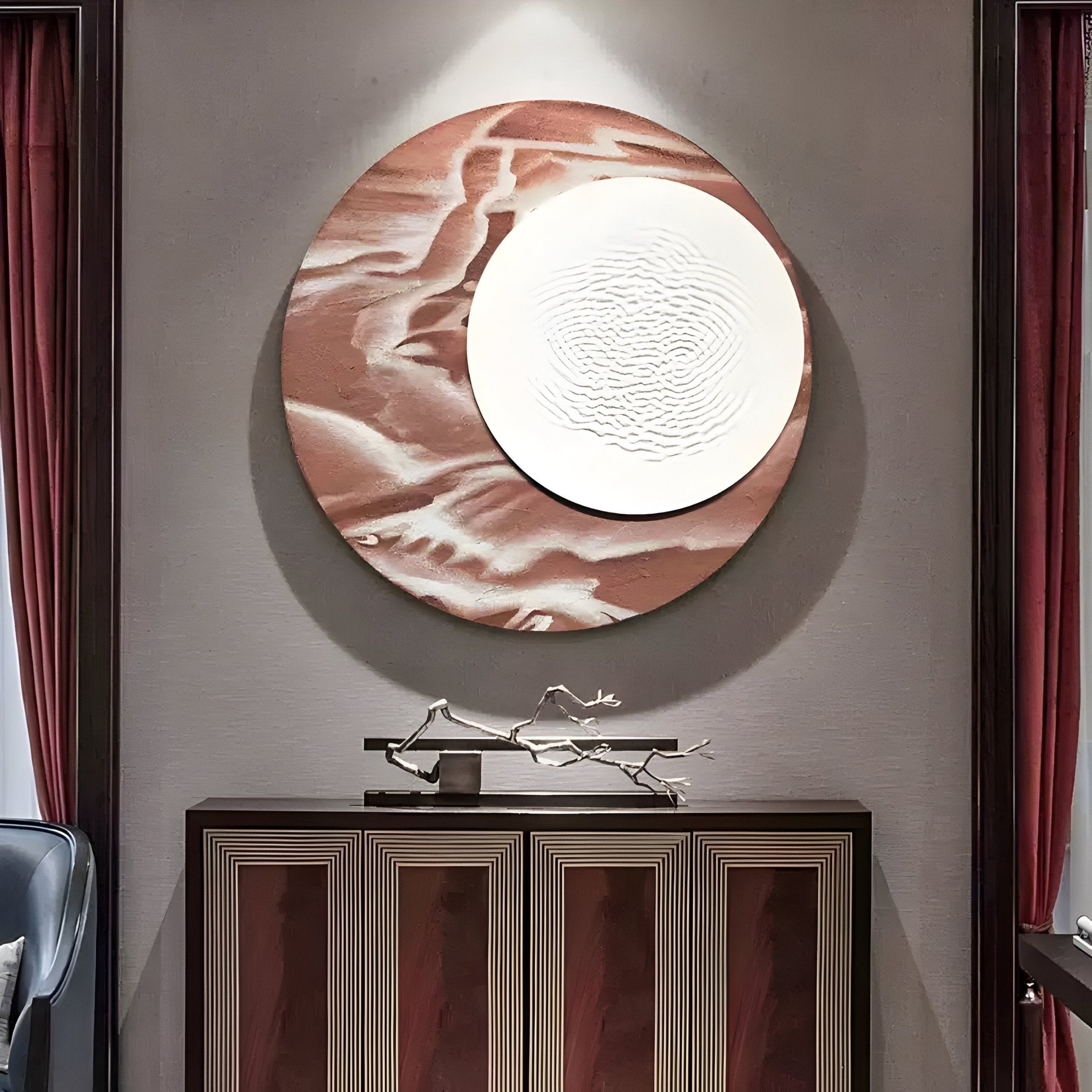 The Reveria Dusty Plum Abstract Wood Carving 3D Wall Art by Giant Sculptures, featuring a large textured circular design in earthy tones, hangs above a wooden cabinet accented with decorative branches and framed by red curtains.