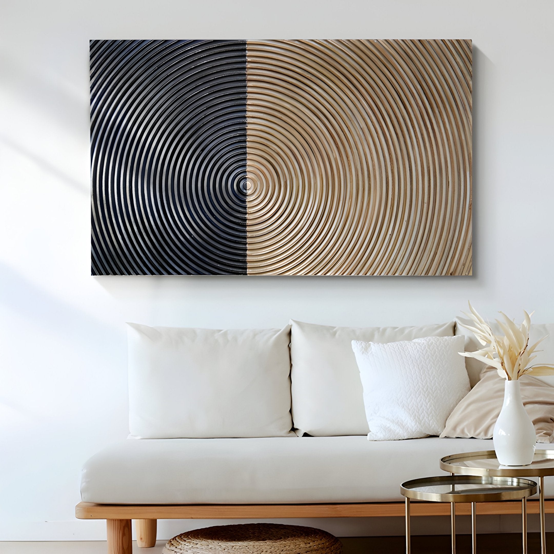 A modern living room with a white couch features the Artura Beige & Black Hand-Painted 3D Relief Wall Art by Giant Sculptures, its bold concentric circles complemented by a minimalist table and vase of dried flowers.