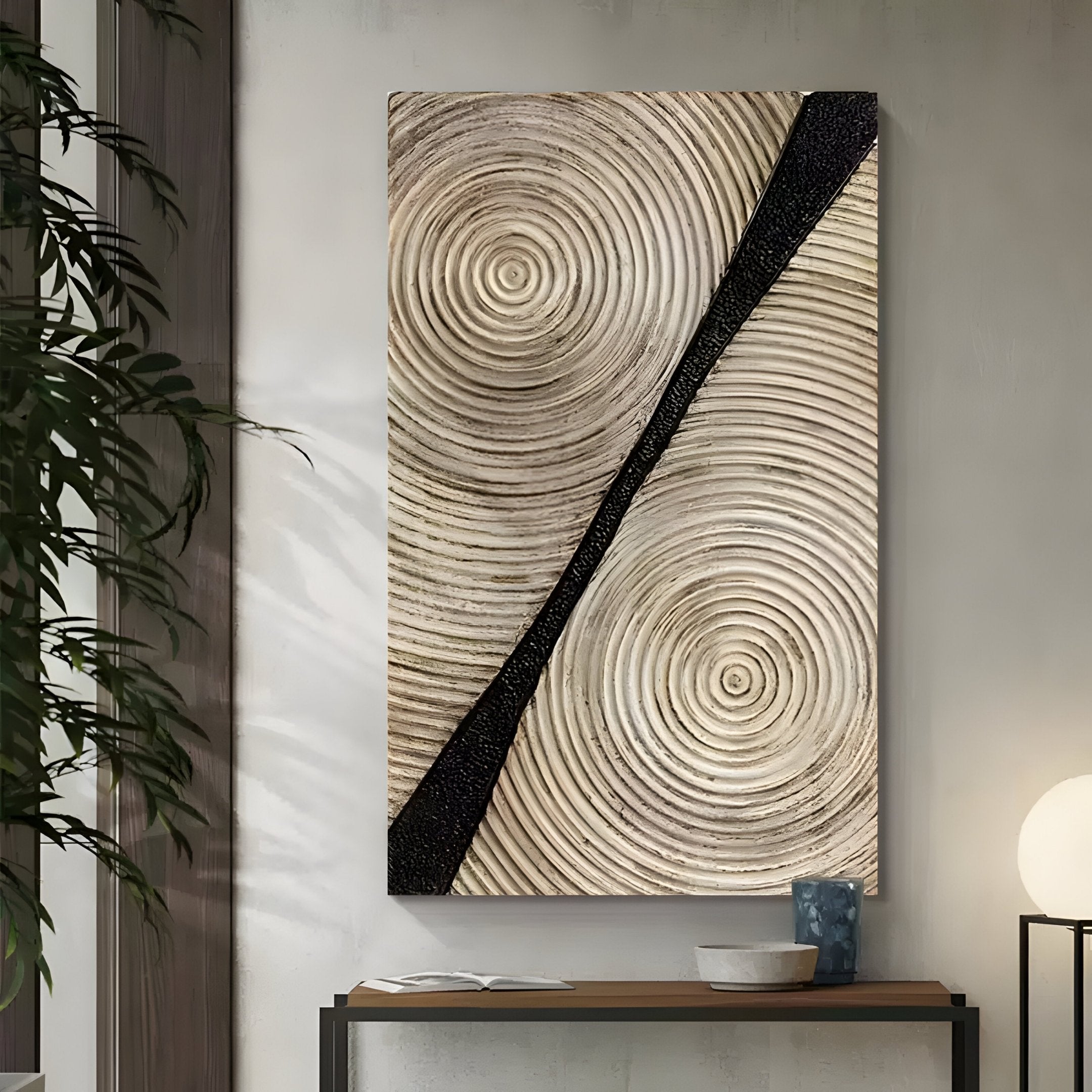 The Artura Ivory Hand-Painted 3D Relief Wall Art by Giant Sculptures features beige concentric circles and a bold black stripe, adding minimalist tranquillity above a console with a bowl, blue vase, plant, and round lamp.