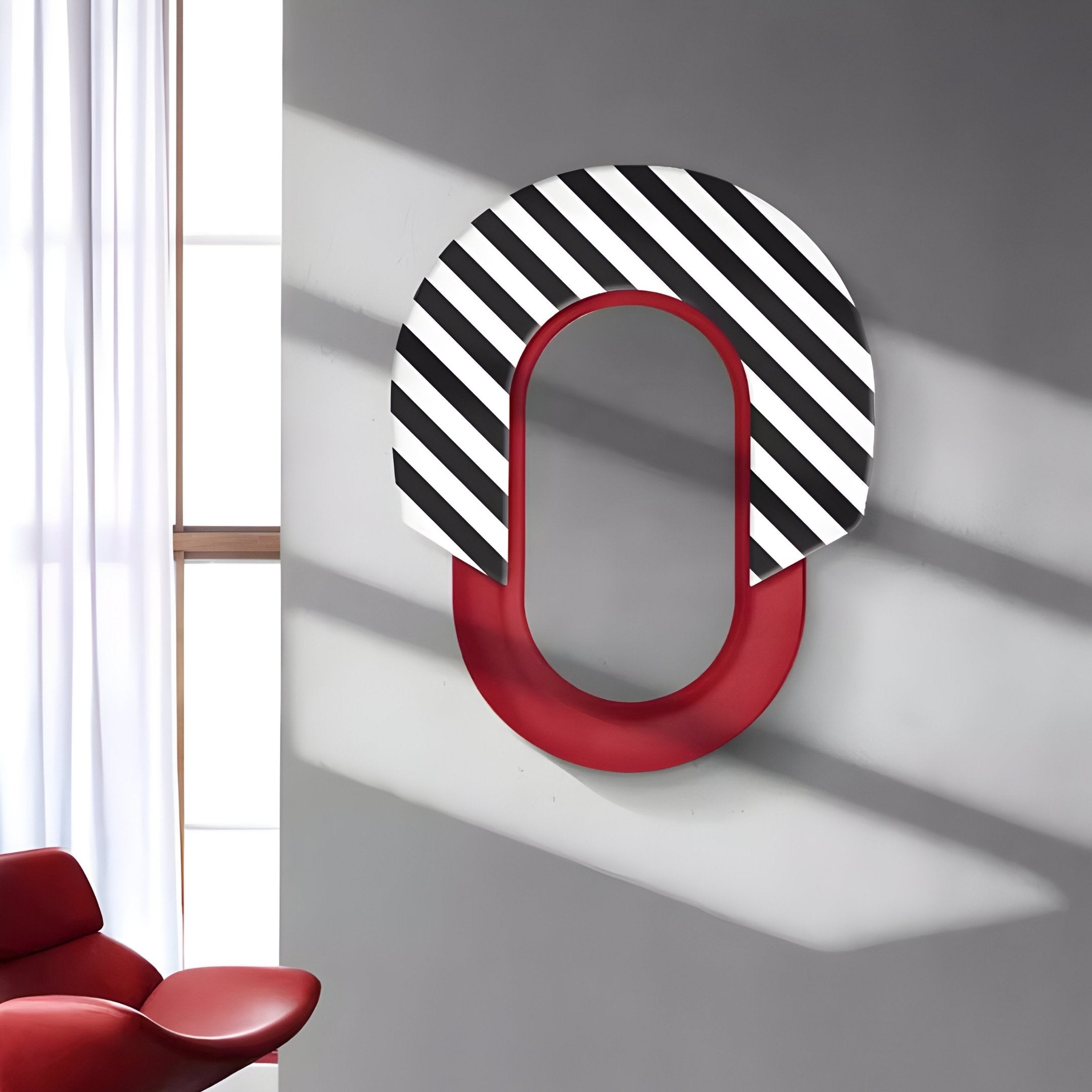 The Arcus Red & Black-White Striped Mirror 3D Wooden Wall Art by Giant Sculptures boasts a modern oval design, perfect for contemporary interiors. Mounted on a gray wall, it casts shadows near a window draped with white curtains and a partially visible red chair in the room.