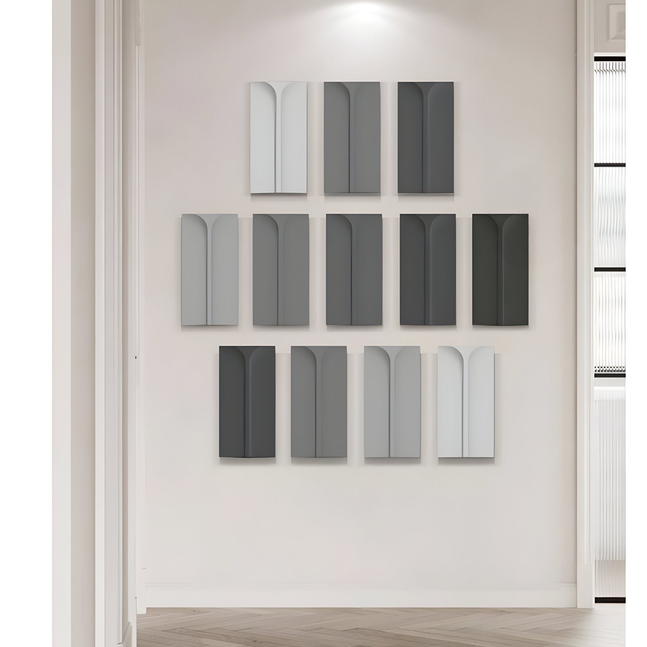 The Eximia by Giant Sculptures is a grayscale multi-panel collection of twelve abstract geometric wood relief pieces with an arch motif, creating a modern, cohesive look on a light-colored backdrop with wood flooring.