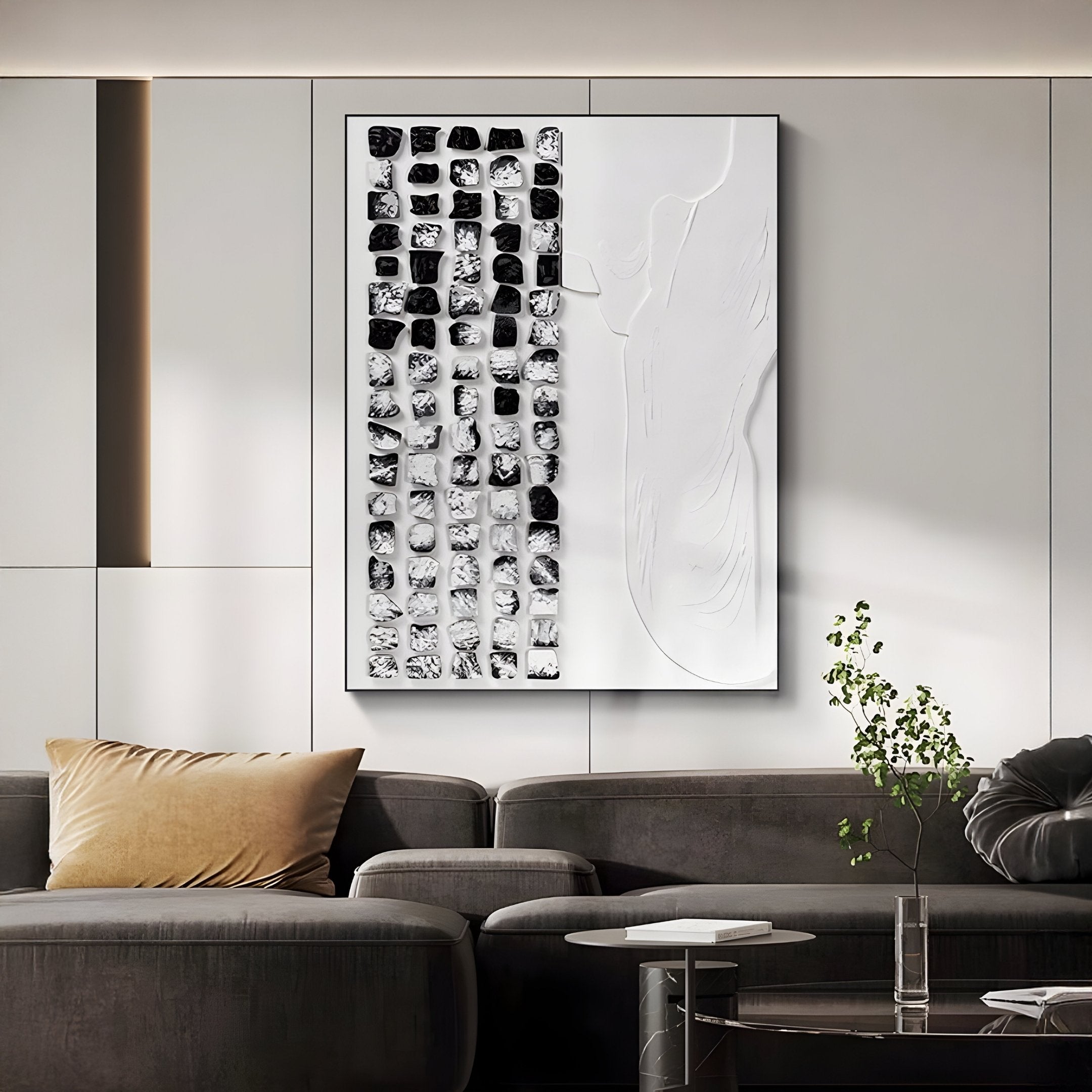 In a modern living room, the Aestilis Black & White Mosaic Wood Carving 3D Wall Art by Giant Sculptures adorns a white paneled wall. A dark gray sofa with a beige pillow enhances the chic look, while a small plant adds natural charm.