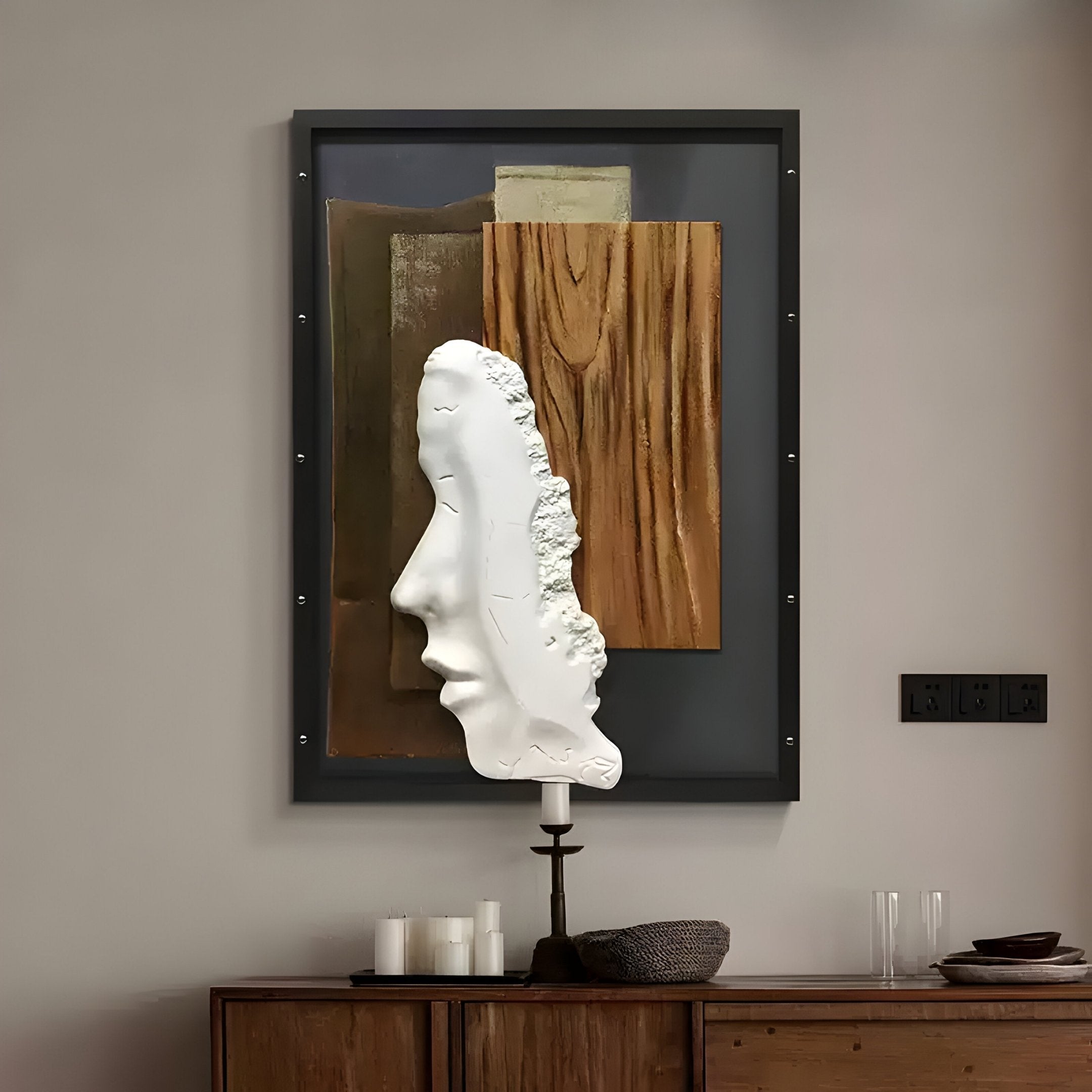 The Visagio Hand-Painted Wood Relief 3D Wall Art by Giant Sculptures features abstract wooden layers with a sculpted profile face. Beneath, a wooden sideboard holds a candle and glassware, while black light switches enhance the room’s Wabi-Sabi feel.