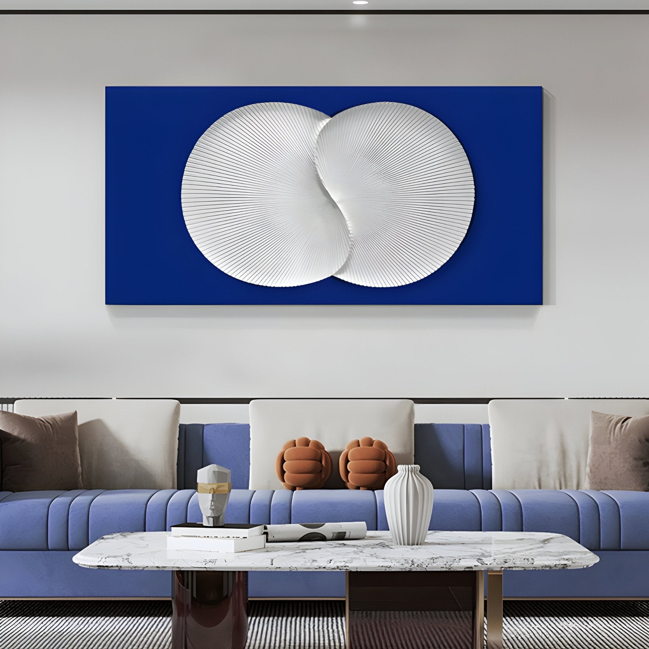 A modern living room with minimalist charm showcases a blue sofa, white cushions, a marble coffee table adorned with a white vase and two brown hand-shaped pillows. Above the sofa hangs the Artivio Blue & White Wood Relief 3D Wall Art by Giant Sculptures, featuring textured blue and white circles.