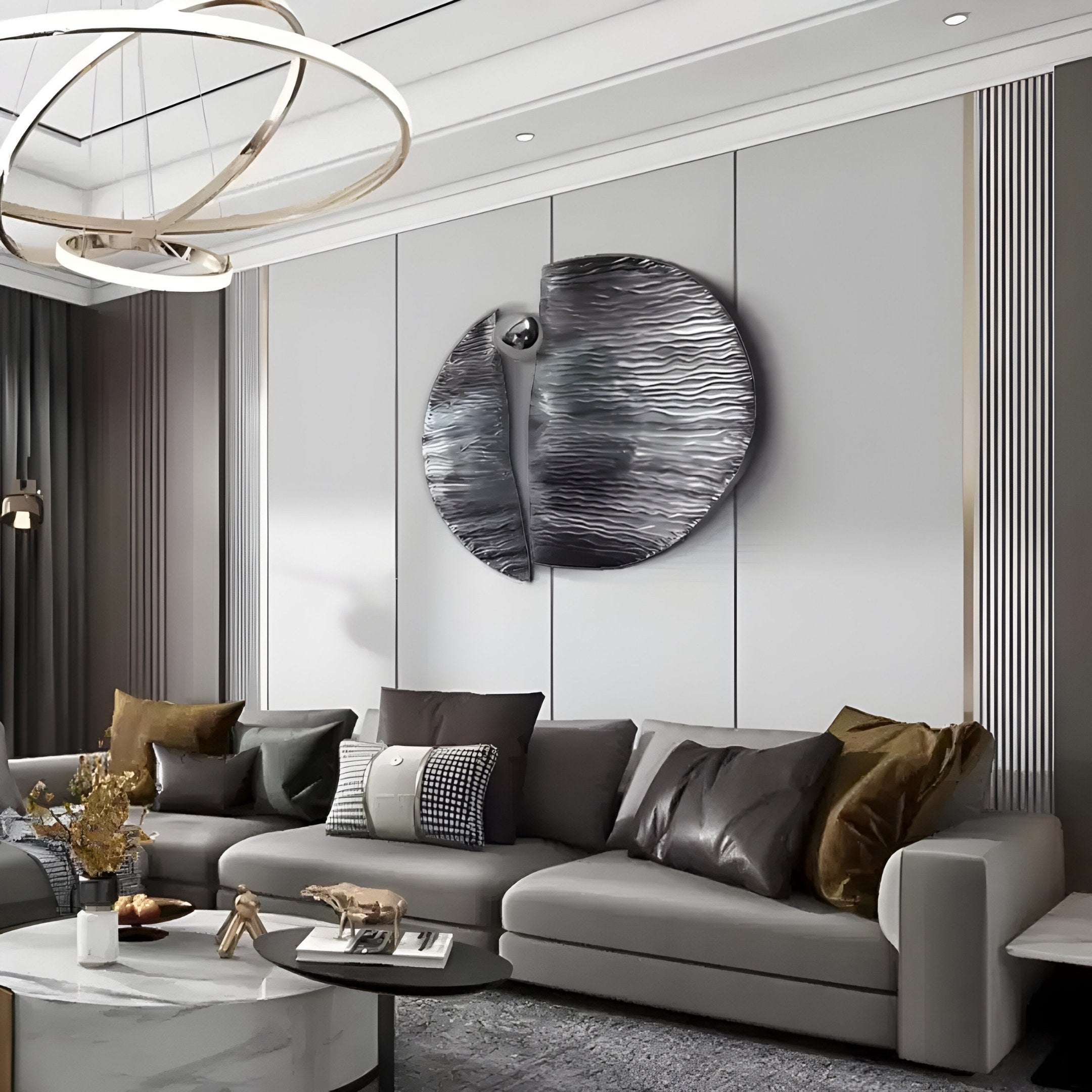A modern living room features a spacious gray sectional with pillows and is highlighted by the Argentum Textured Wood Relief 3D Wall Art With Silver Metal Ball by Giant Sculptures on the gray wall. A round coffee table below a contemporary chandelier completes the neutral-toned setting.
