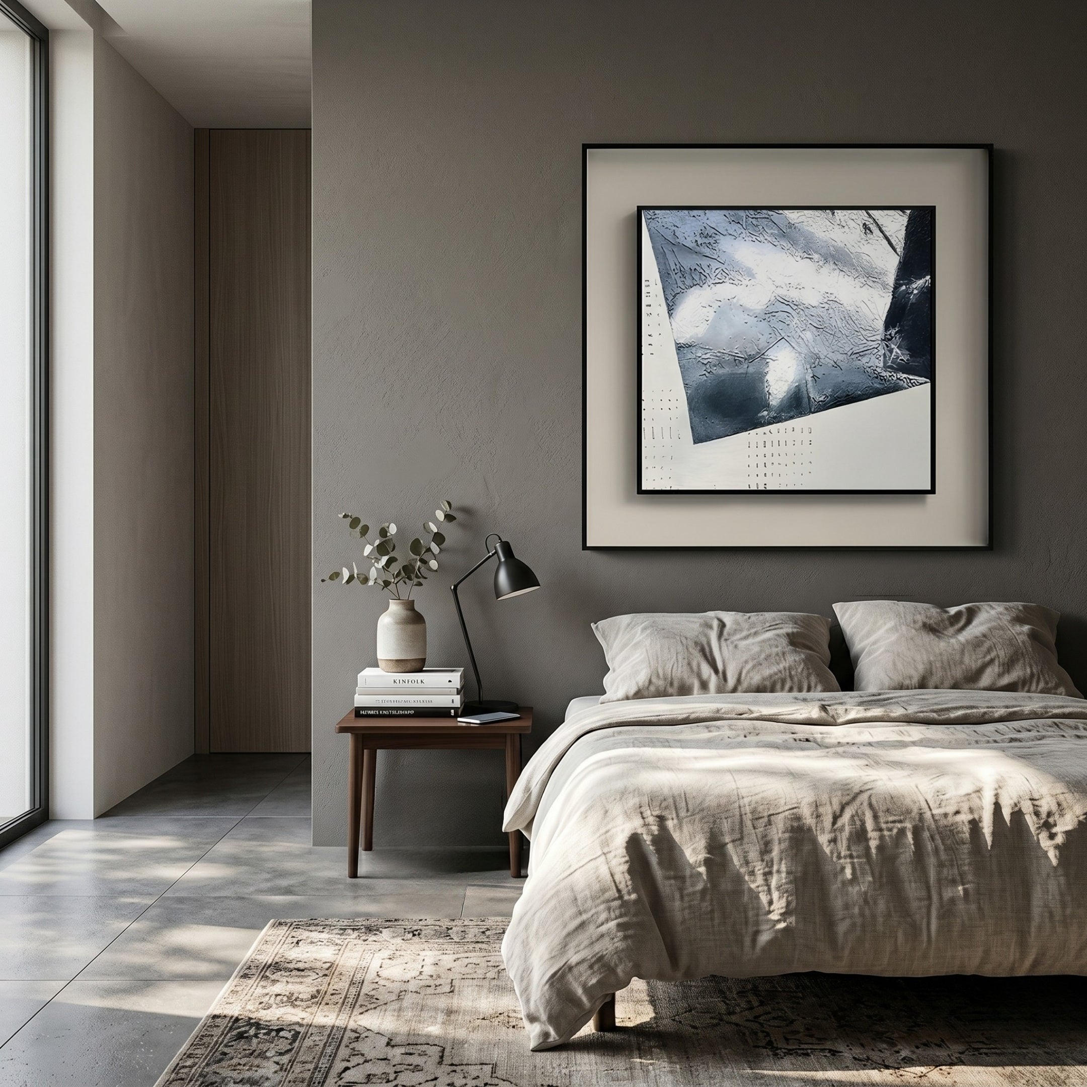 A modern bedroom with gray walls showcases the Stratonis Silver Folded Plane Textured Framed Wall Art by Giant Sculptures above a neatly made bed, beside a wooden nightstand with books, lamp, foliage-filled vase, and a patterned rug in natural light.
