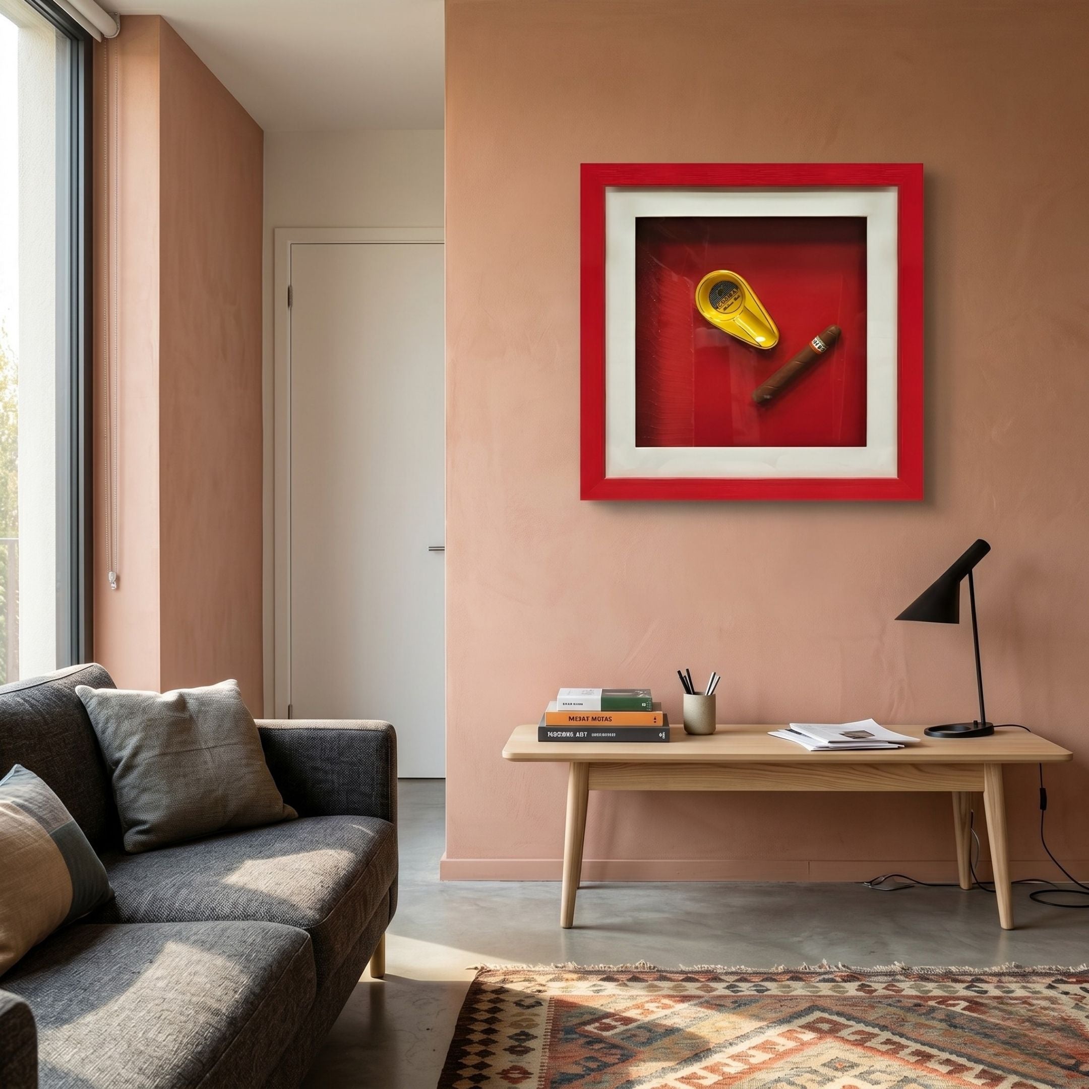 A modern living room features a gray sofa, wooden table with books and black lamp, and is accented by Giant Sculptures' Cavendro Gold Ashtray & Cigar Framed Wall Art displayed on a pink wall.
