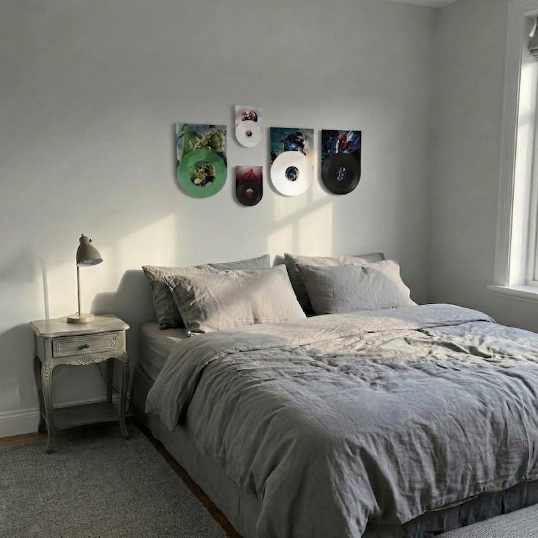 ReelRiot Comic Legends Record 5-Panel Wall Art by Giant Sculptures displayed above a grey bed in a minimal bedroom, featuring green, white, red, and black vinyl record panels with comic character prints.