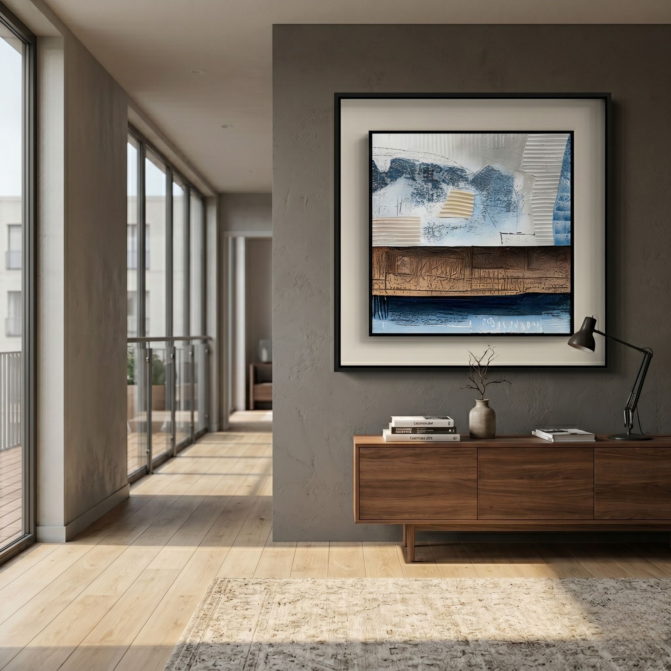 Aerolith Blue & Earthy Abstract Textured Framed Wall Art by Giant Sculptures hung above a walnut console in a modern hallway with floor-to-ceiling windows.