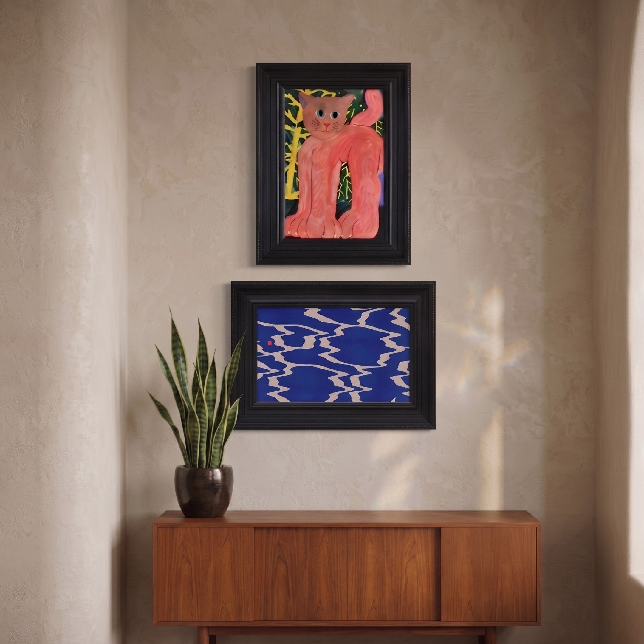 Ardensir Pink Cat & Blue Ripple 2-Set Framed Wall Art by Giant Sculptures displayed on a textured beige wall, featuring a pink cat painting above a blue ripple print in ornate black frames, styled above a walnut sideboard with a snake plant.