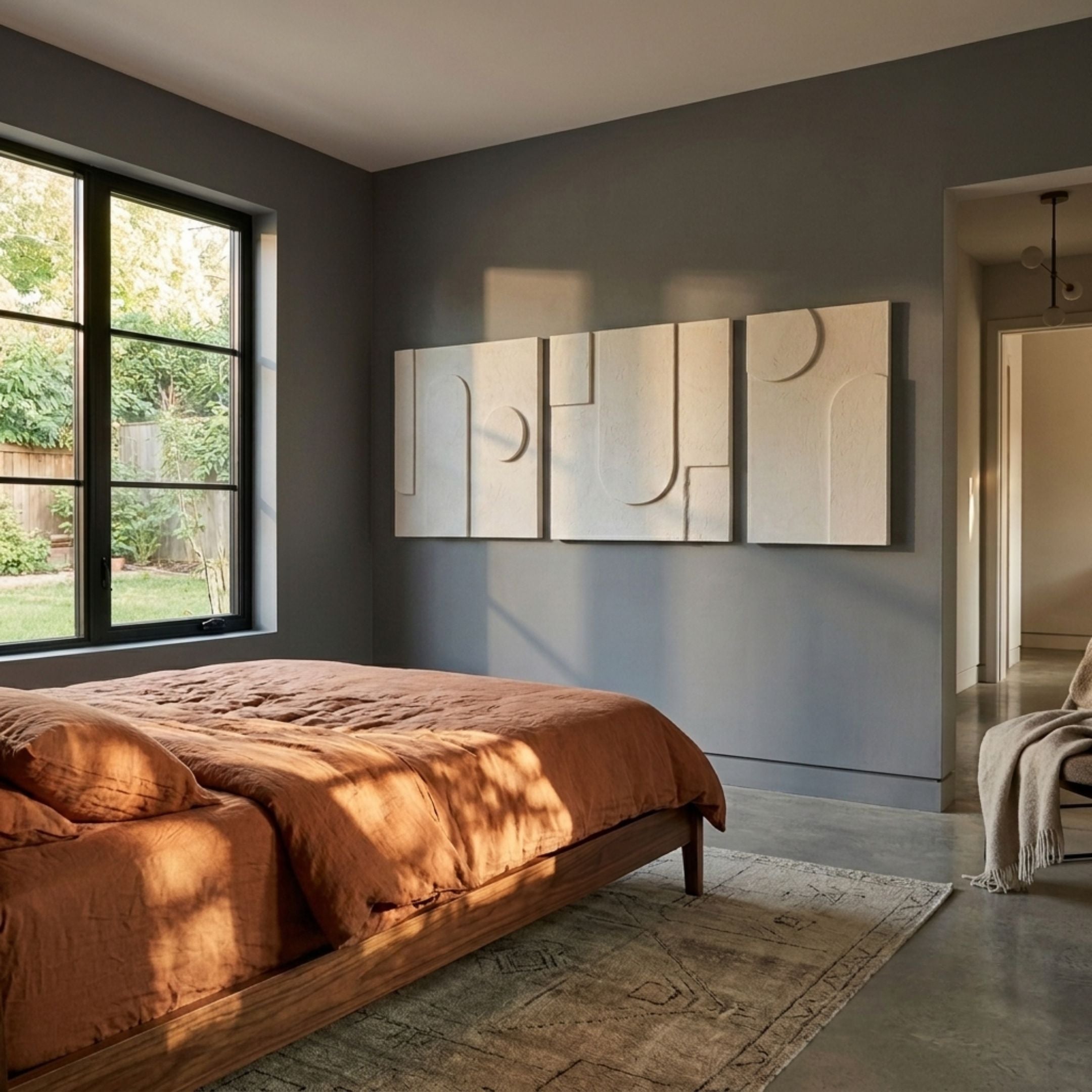 Moro III Triptych Sandstone Relief 3D Wall Art by Giant Sculptures displayed above a wooden bed with rust linen bedding in a grey-walled modern bedroom.