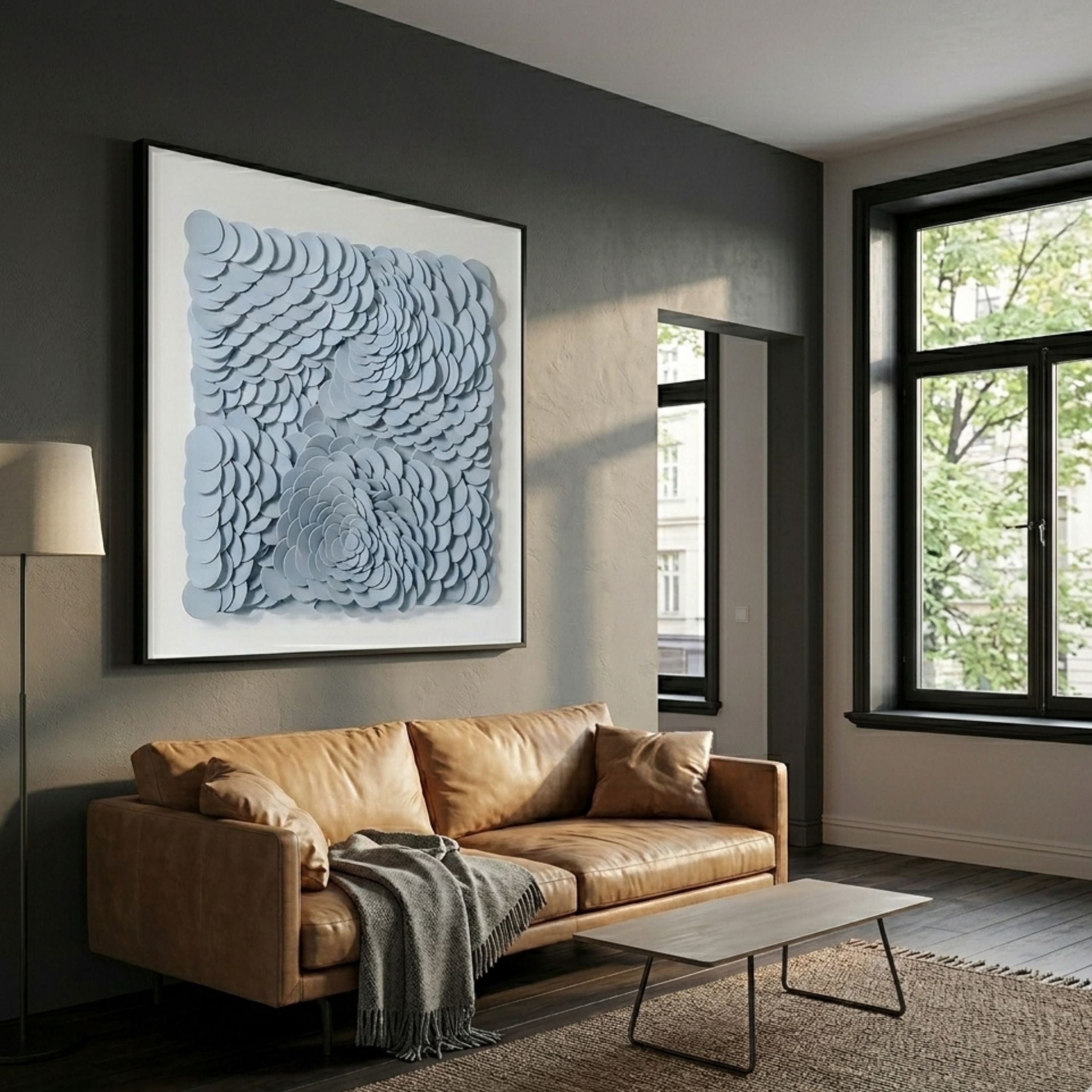 Calavine Blue Bloom Sculptural Leather 3D Wall Art in powdery blue with black frame, displayed above a tan leather sofa in a modern grey living room.