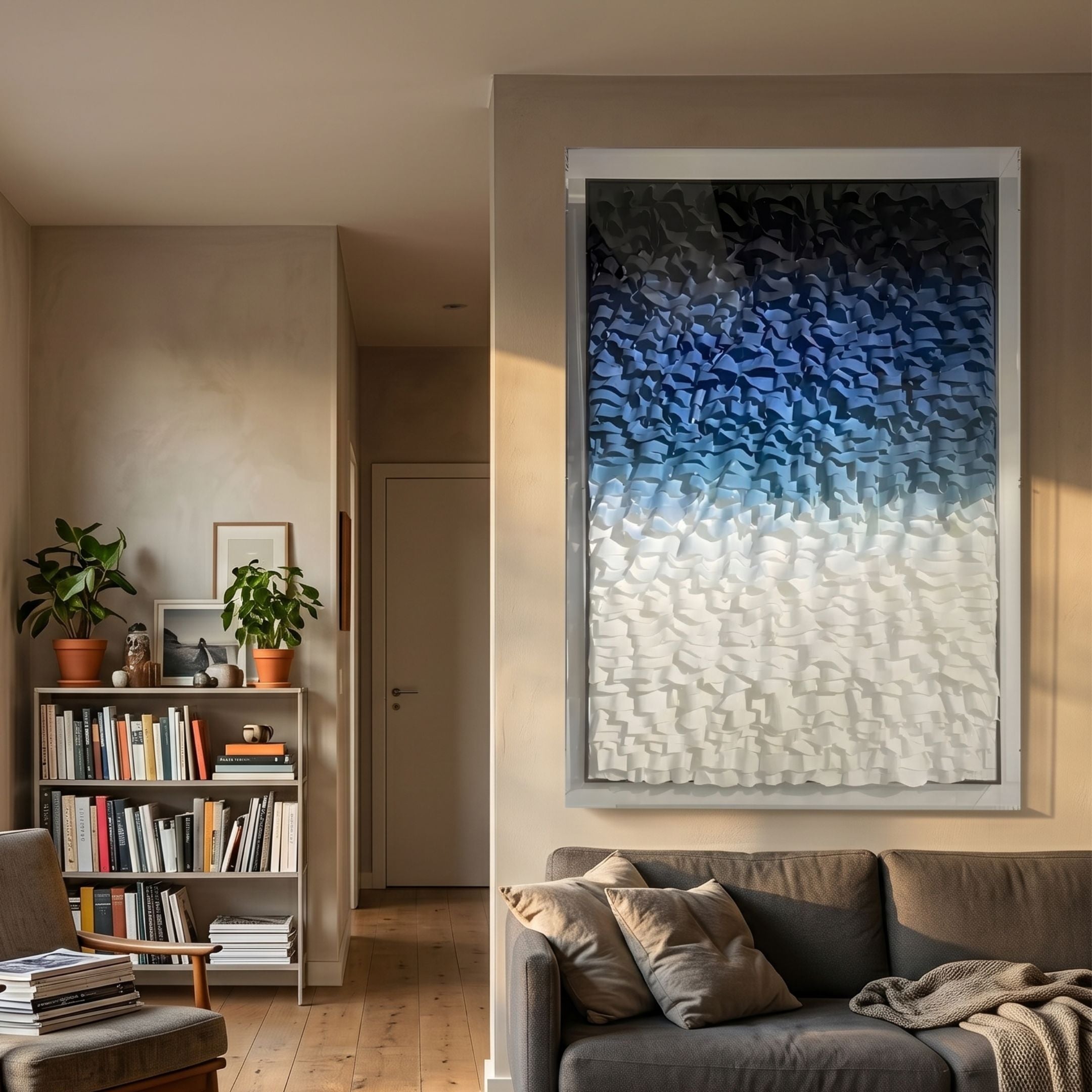 Vistra Navy & Sky Blue Ombre Ruffled 3D Paper Wall Art in acrylic box frame above a grey sofa, beside a bookshelf with plants in a sunlit living room.