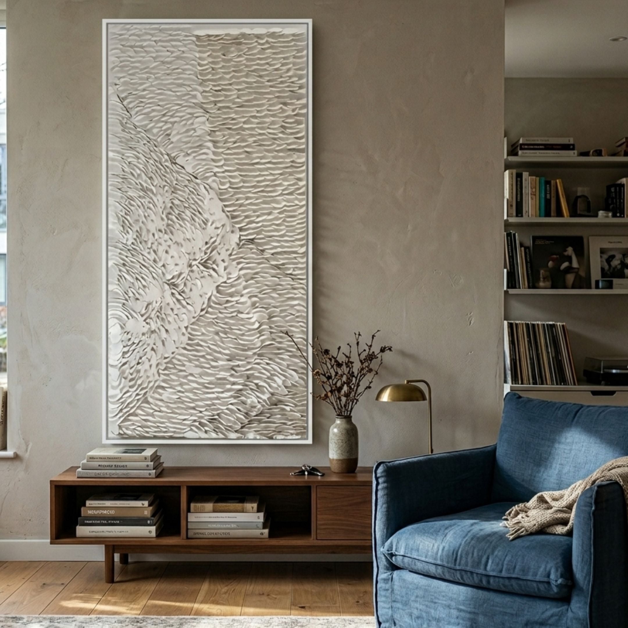 Vermira Ivory I Textured Leather 3D Wall Art by Giant Sculptures mounted above a walnut console in a living room with a blue armchair and bookshelves.