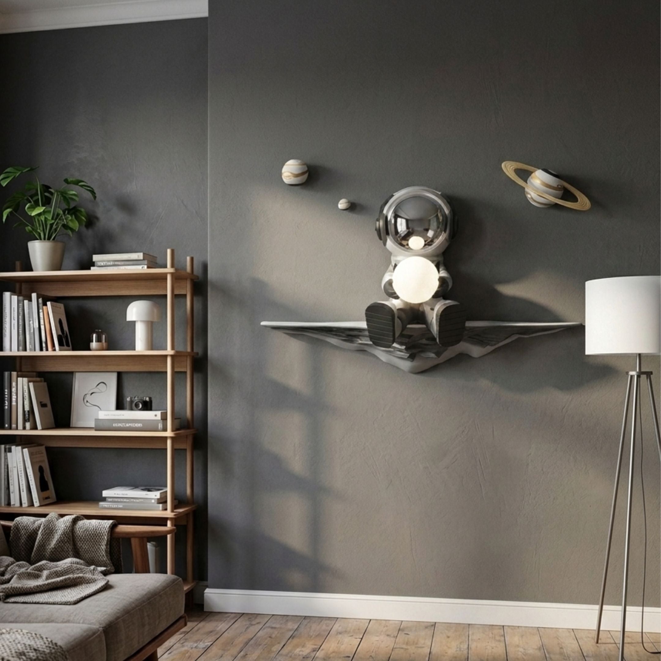 Silver 3D Dreamer Glow Astronaut Wall Art by Giant Sculptures, mounted on a grey living room wall with planets and a glowing orb, near a bookshelf and floor lamp.