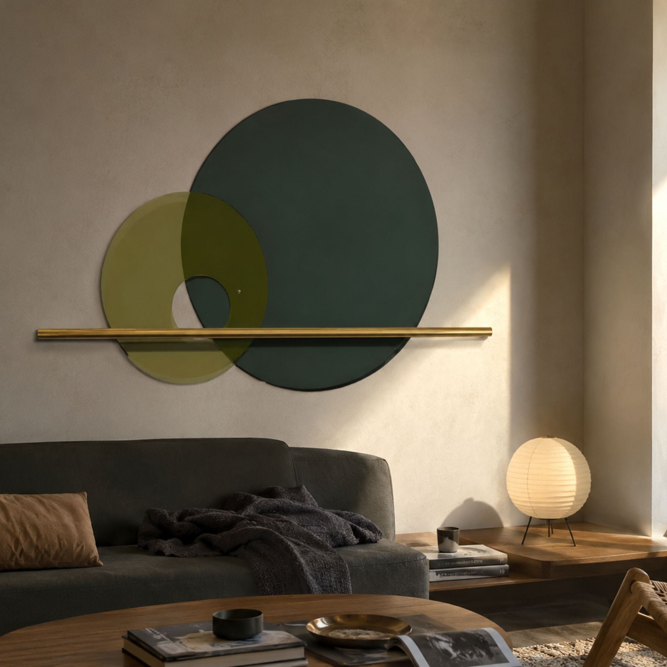 Luna Forma Forest Green Round Brass Accent Wall Art with overlapping translucent discs and a horizontal brass rod, displayed above a grey sofa in a living room.
