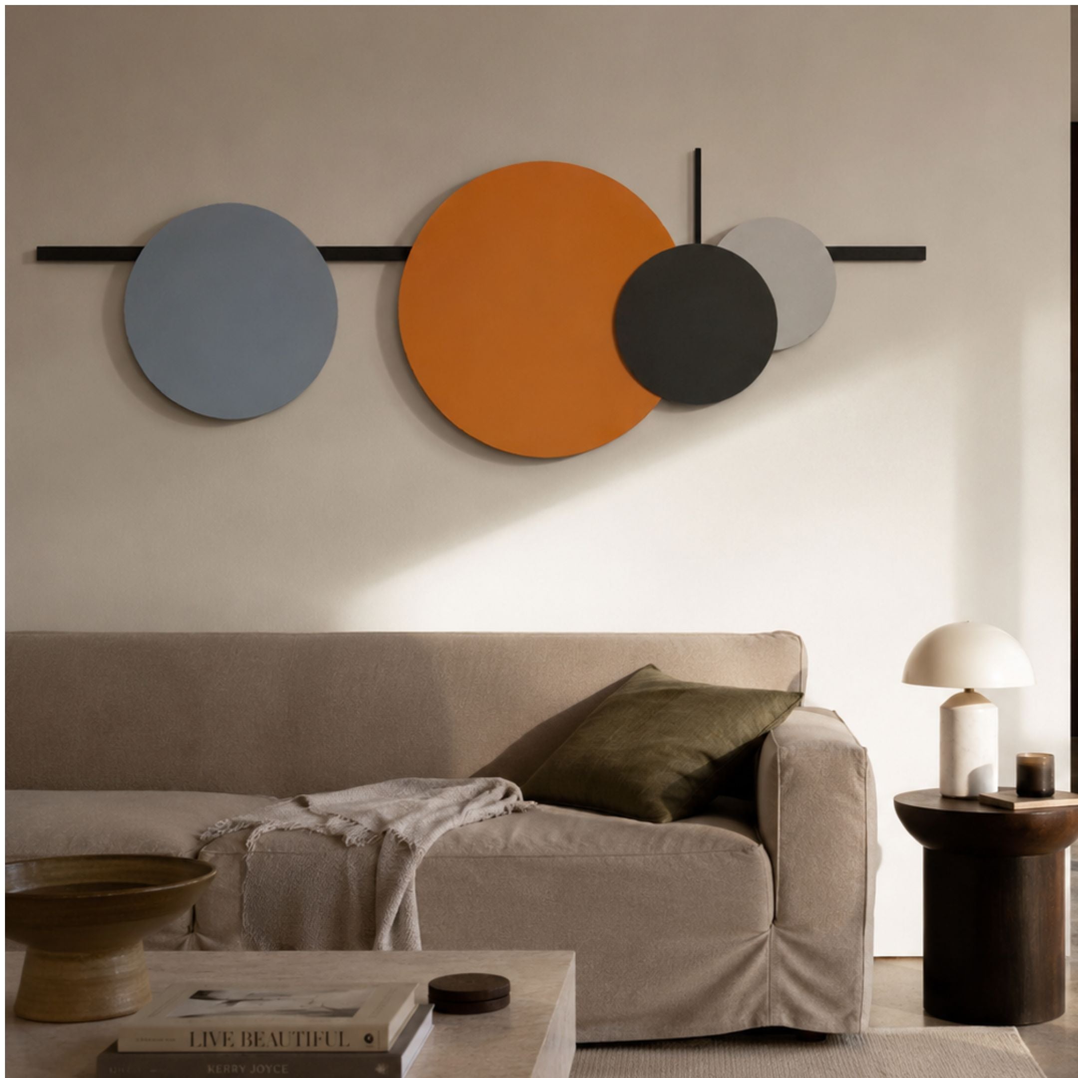 Orbit III Dynamic Flow Multicoloured Circular Wall Art by Giant Sculptures, with blue, orange, black, and grey discs on black linework above a beige sofa.
