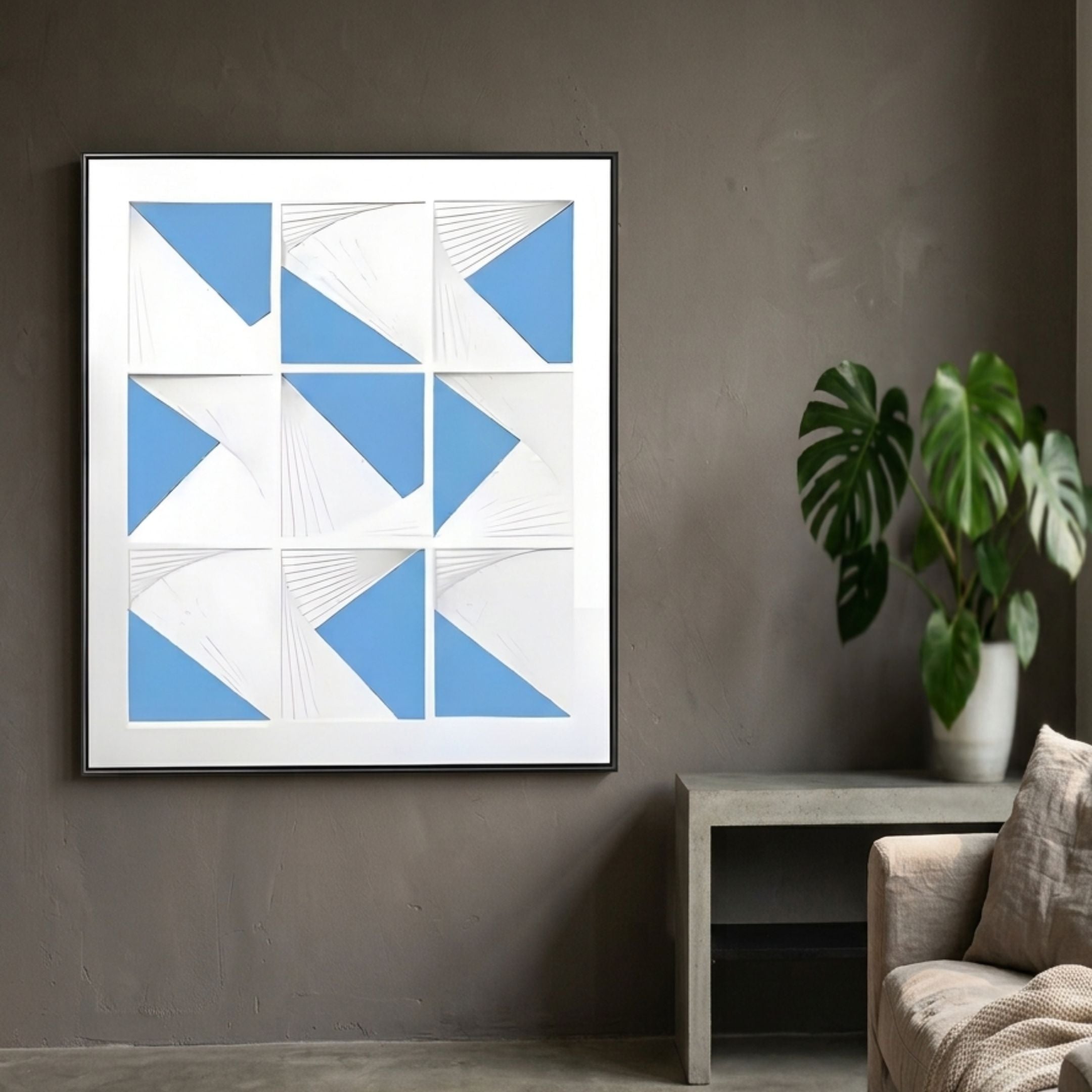 Prismatics Blue Geometric Cardboard Wall Art by Giant Sculptures, a 3×3 grid of white panels with blue triangles, displayed on a grey wall above a concrete bench.