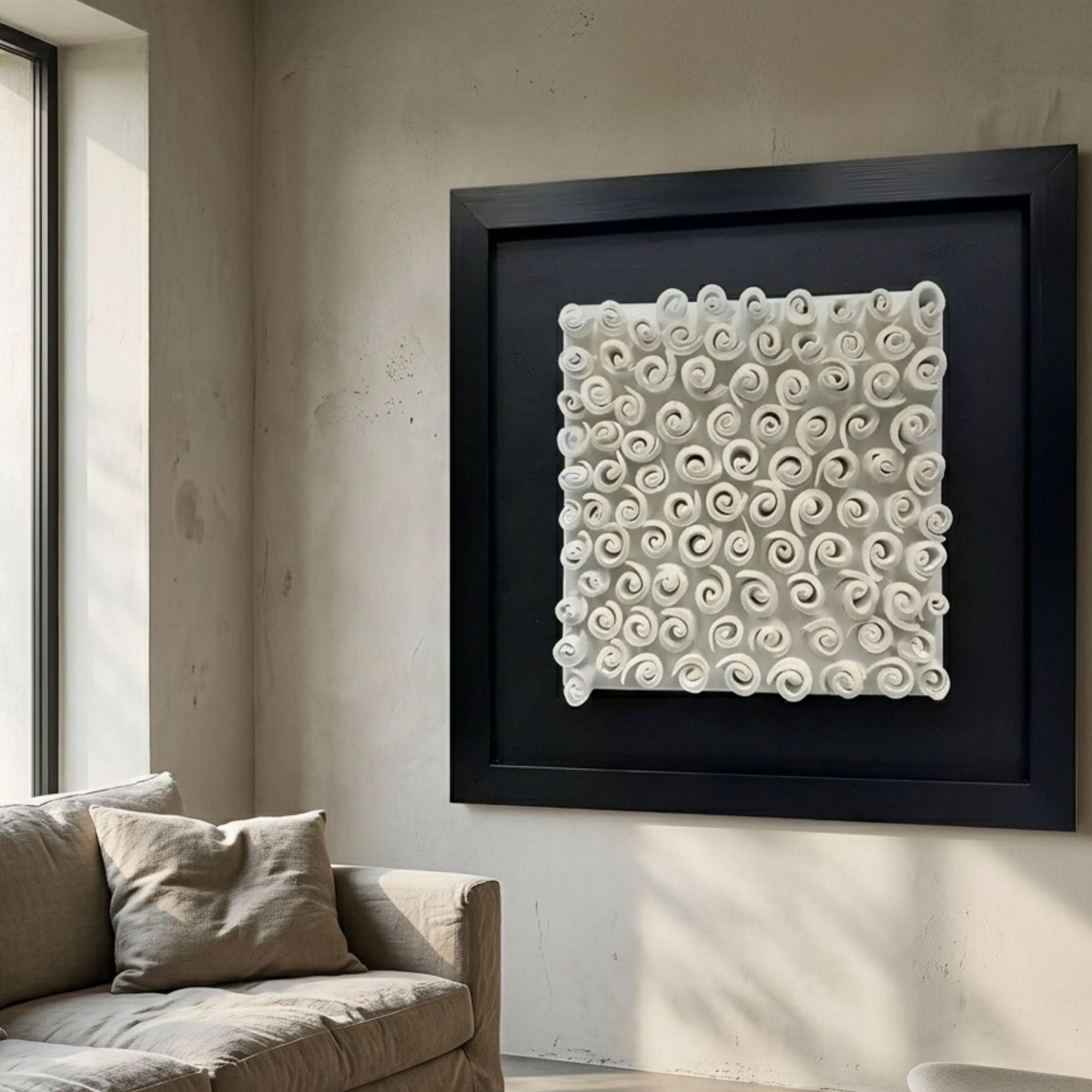 Harmonia 3D Spiral Ceramic Wall Sculpture with black frame displayed above a beige sofa in a sunlit minimalist living room with pale plaster walls.