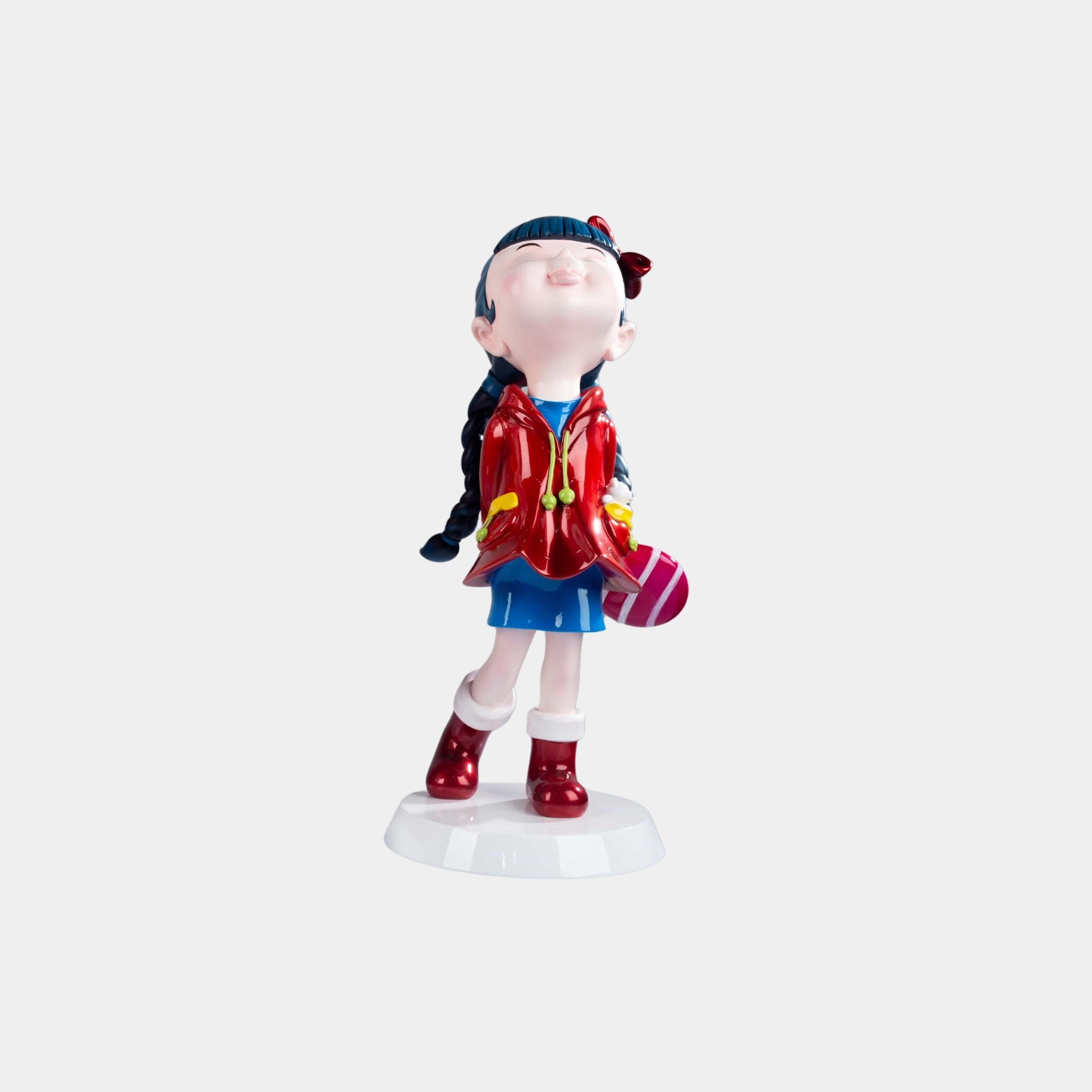 The Cherry Red Lulabelle Figure - 20cm by Giant Sculptures is crafted from eco-friendly polyurethane, showing a girl in a red jacket and blue skirt with blue braided hair, pink striped purse, joyful gaze, and stands on a white base.