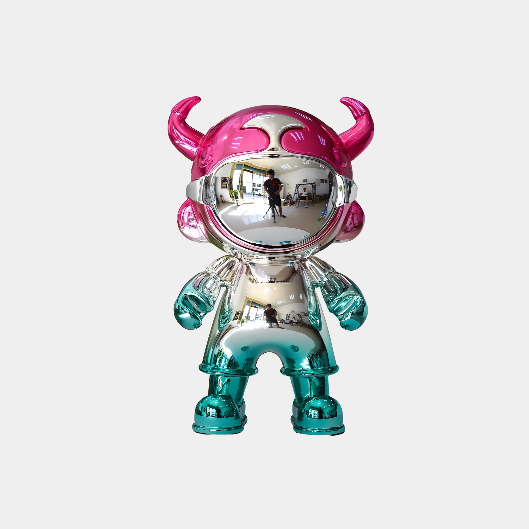 The Giant Sculptures Pink & Teal Electroplated Astro Devil Figure (35cm) features a chrome-like teal body, pink horned helmet, and teal gloves and boots—reflecting surroundings and ideal as a collectible art piece.